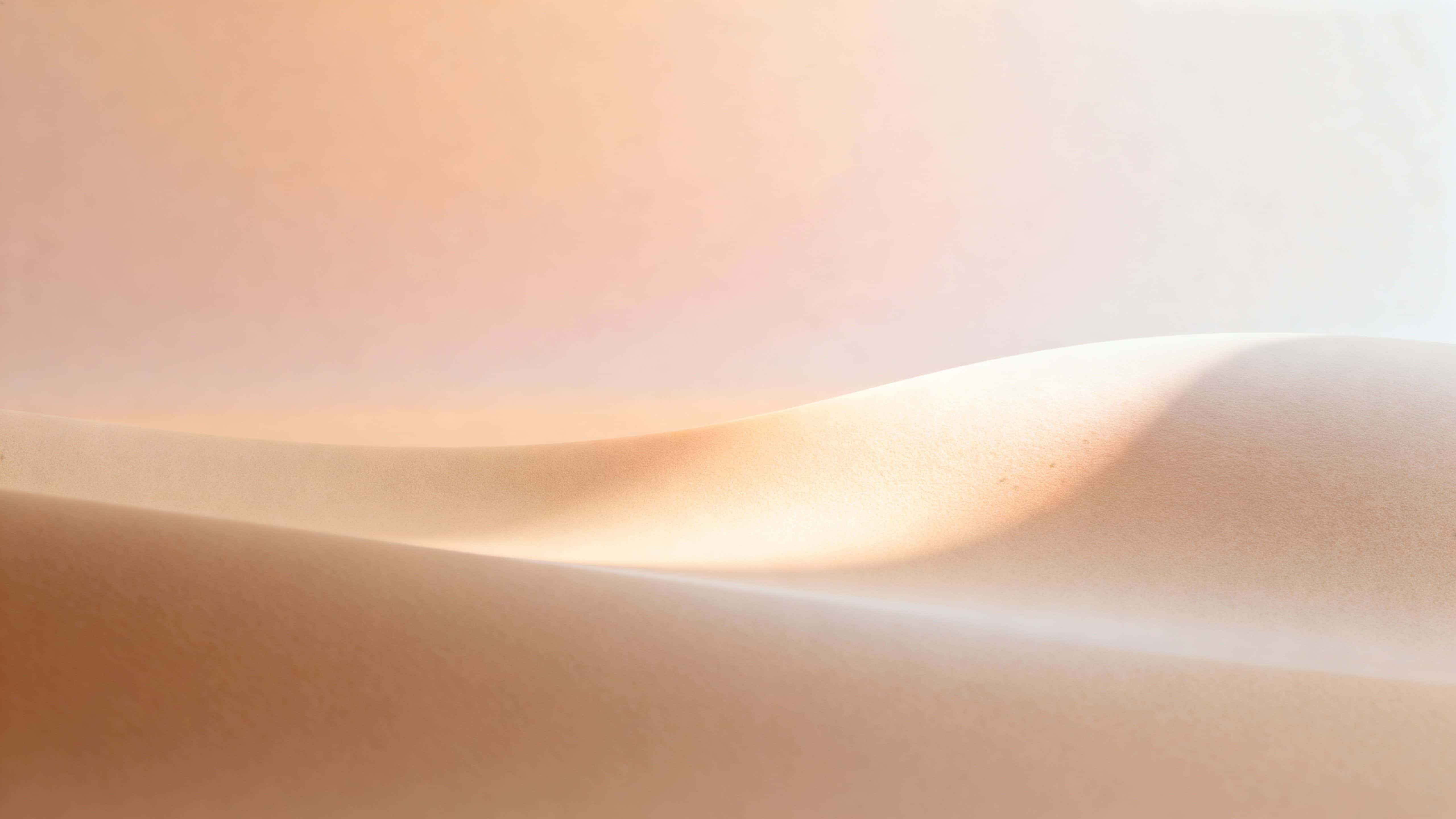 A minimalist 16:9 view of an infinite matte color plane where warm sand-beige rises into pale apricot and creamy blush via a soft atmospheric fade, with a subtly luminous bulge slightly right of center.