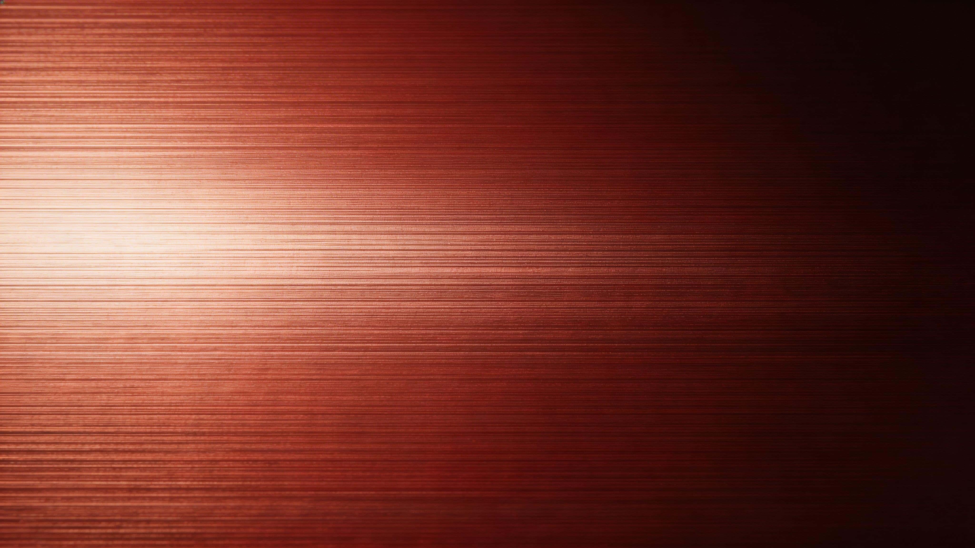 Studio product photograph (16:9) of a subtle brushed red metal surface with fine horizontal grain, soft directional highlights fading into deep shadow and a clean negative space.
