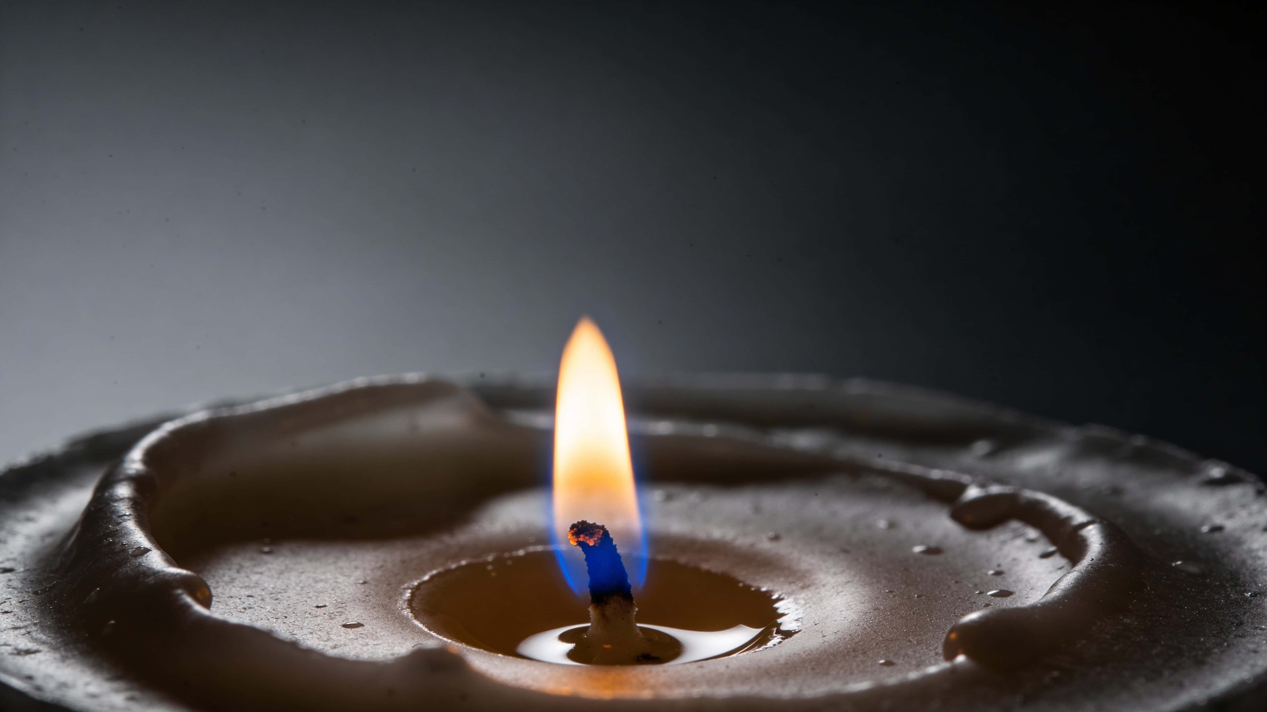 Single candle flame captured as a low-key fine-art photograph in total darkness, composed and cropped for a 16:9 wallpaper or poster with serene mood and rich warm tones.