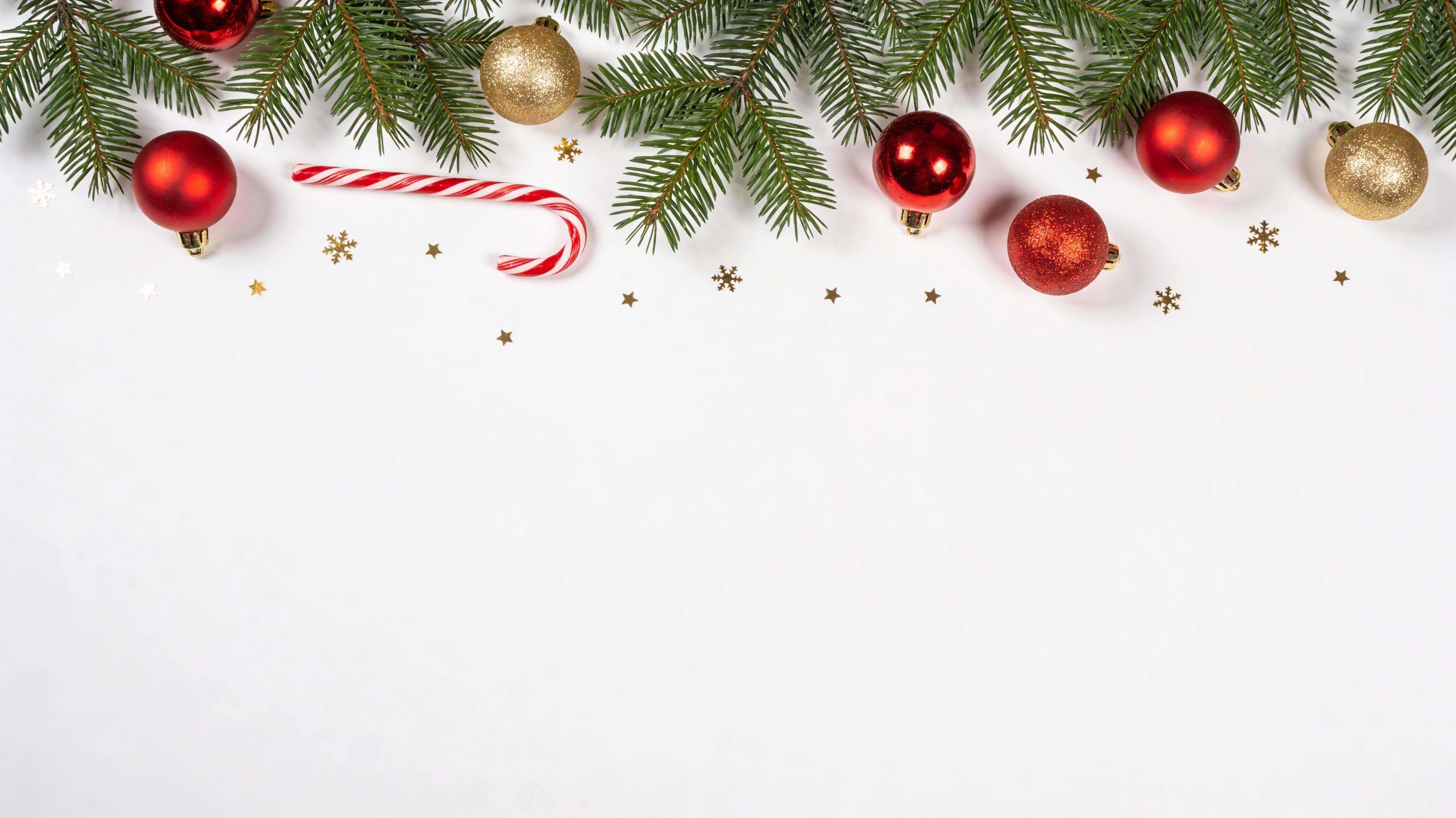 Top-down 16:9 flat-lay of a minimal Christmas border on pure white, with sparse pine greenery at the top, a few red and gold ornaments, a single candy cane and subtle gold snowflake confetti, leaving the center empty.