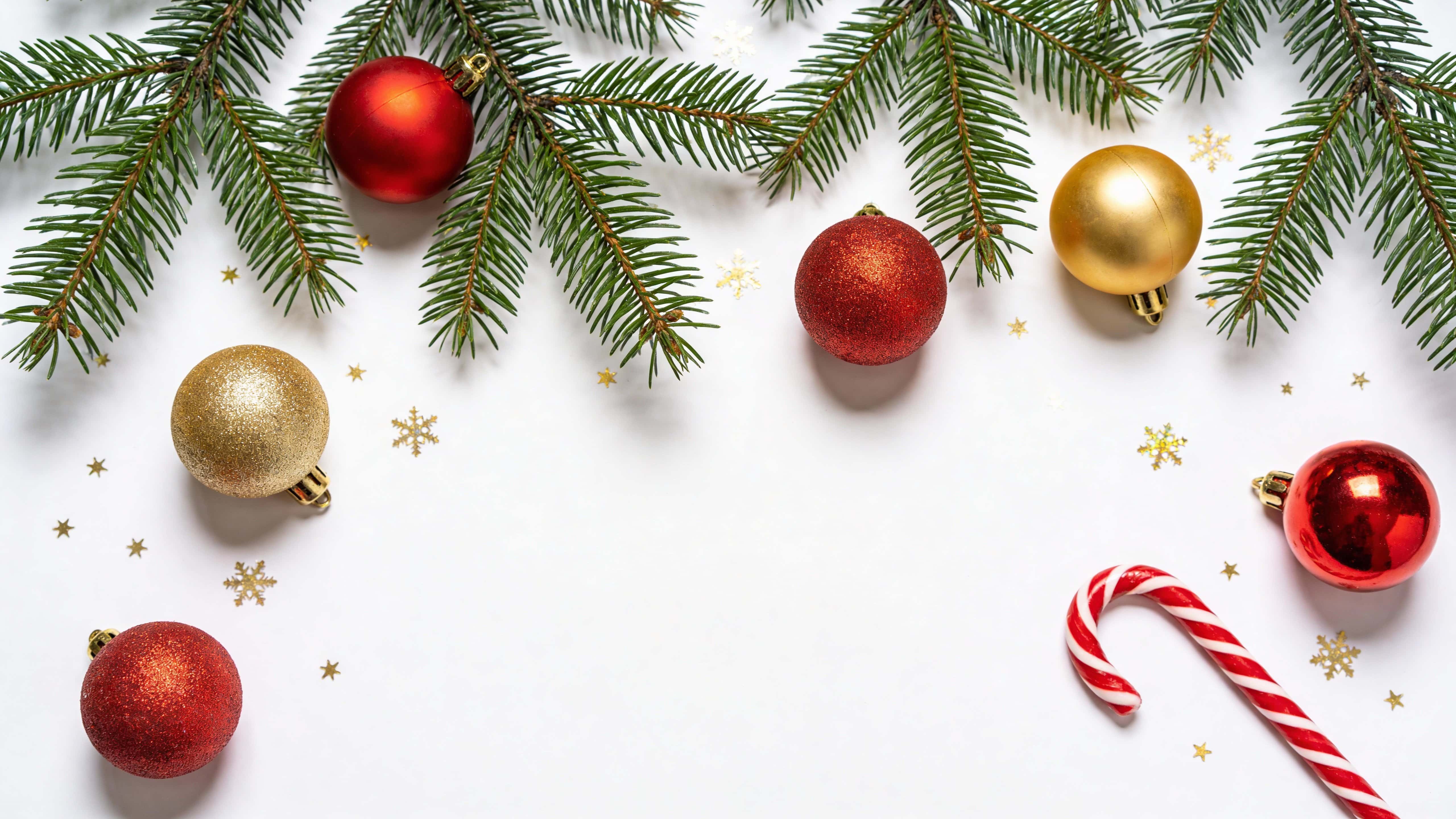 Top-down 16:9 flat lay border of sparse pine greenery, a few red and gold ornaments and a single candy cane with subtle gold snowflake confetti on a pure white background.