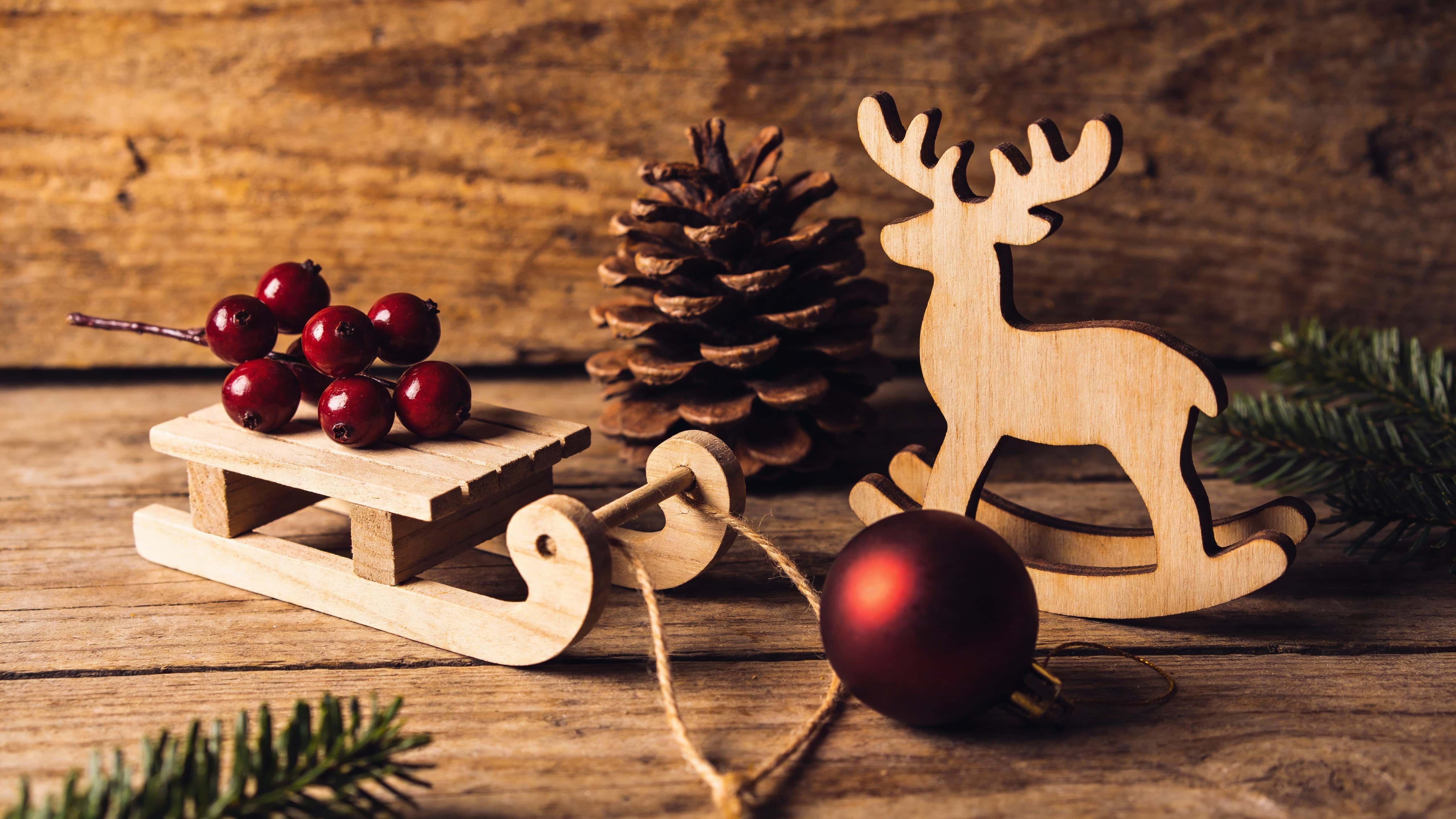 A 16:9 tabletop still life photograph emphasizing rich wood grain, matte ornaments, and an earthy, rustic Christmas palette and mood.