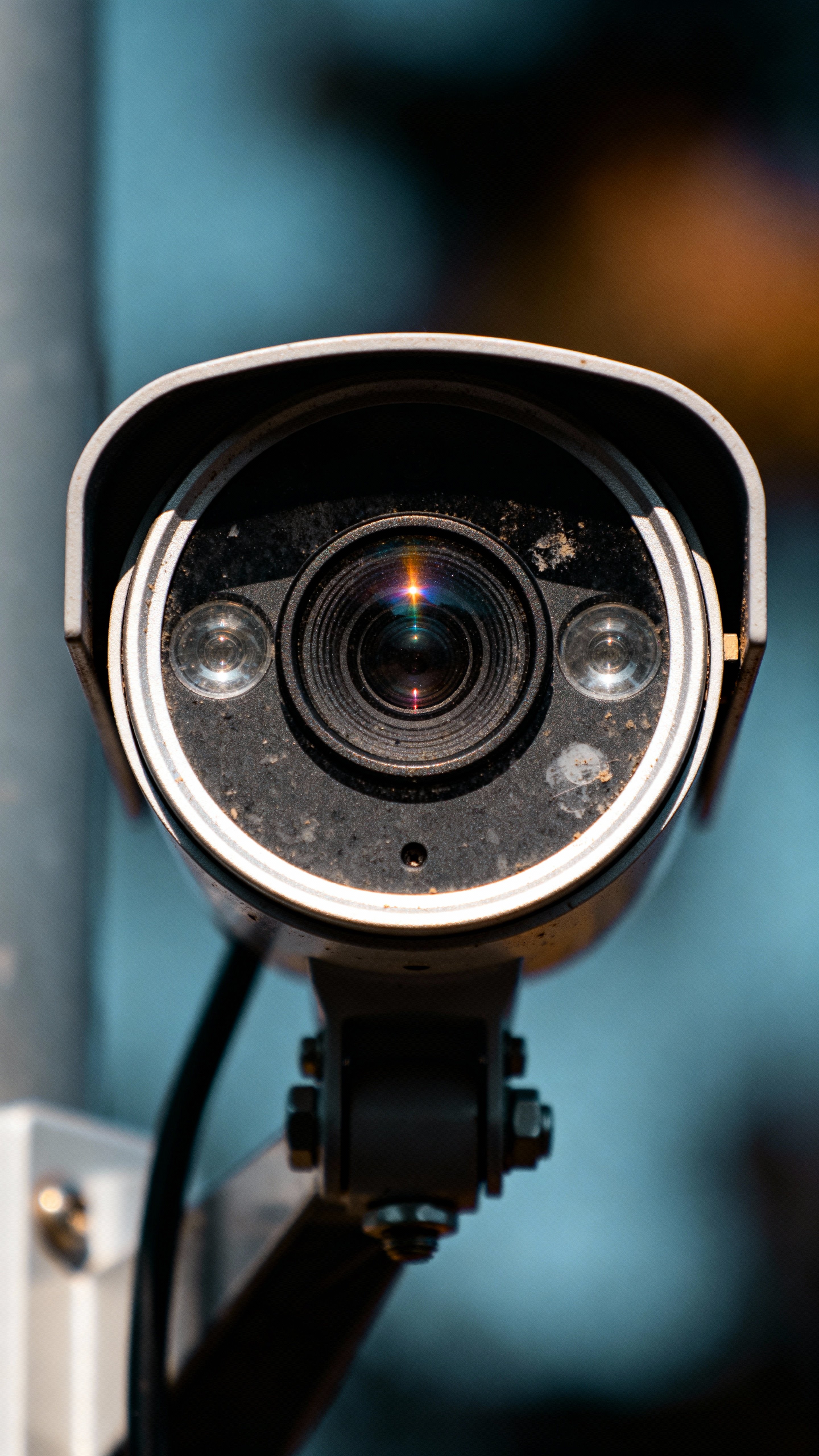 Close-up, cinematic, realistic photograph of a CCTV security camera mounted centrally and staring directly forward. Emphasize lens reflections, fine mechanical detail, subtle weathering, and dramatic lighting for an artistic and creative,电影