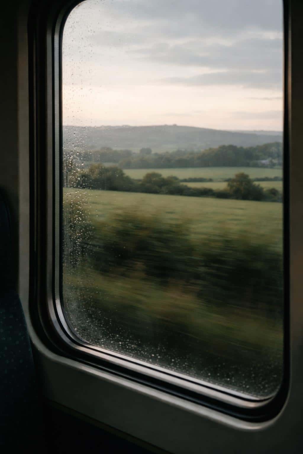 A vertical 2:3 photographic scene of countryside seen through a moving train window, composed for wallpaper or poster with cinematic motion blur, soft light and layered depth.