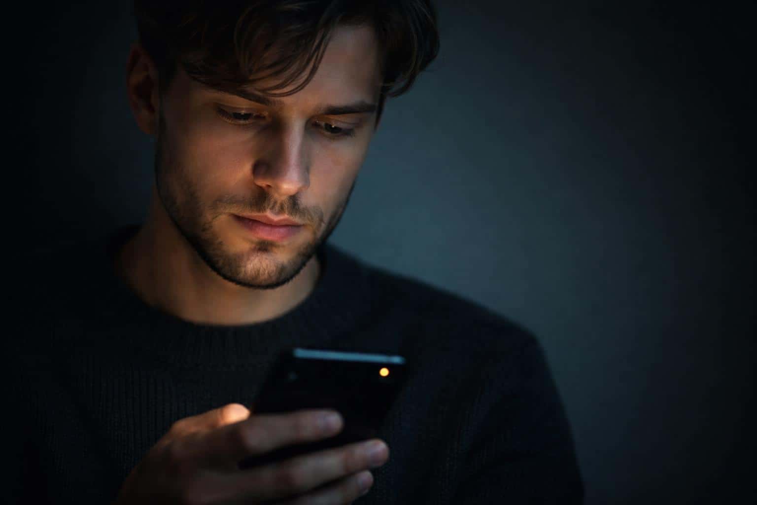 Close-up portrait of a creator staring at a phone, photographed with low notification glow and intimate low-key lighting for a social-post hero image.