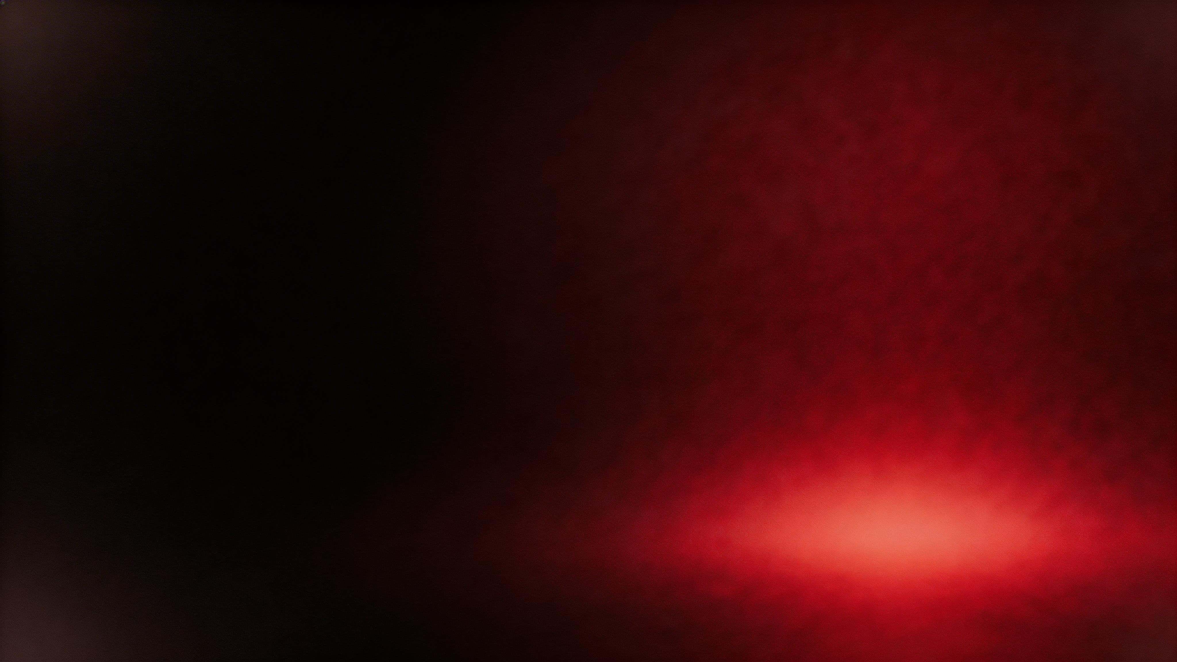 16:9 abstract widescreen wallpaper with a deep crimson light basin blooming into near-black corners, matte texture, restrained film grain, and asymmetric negative space.