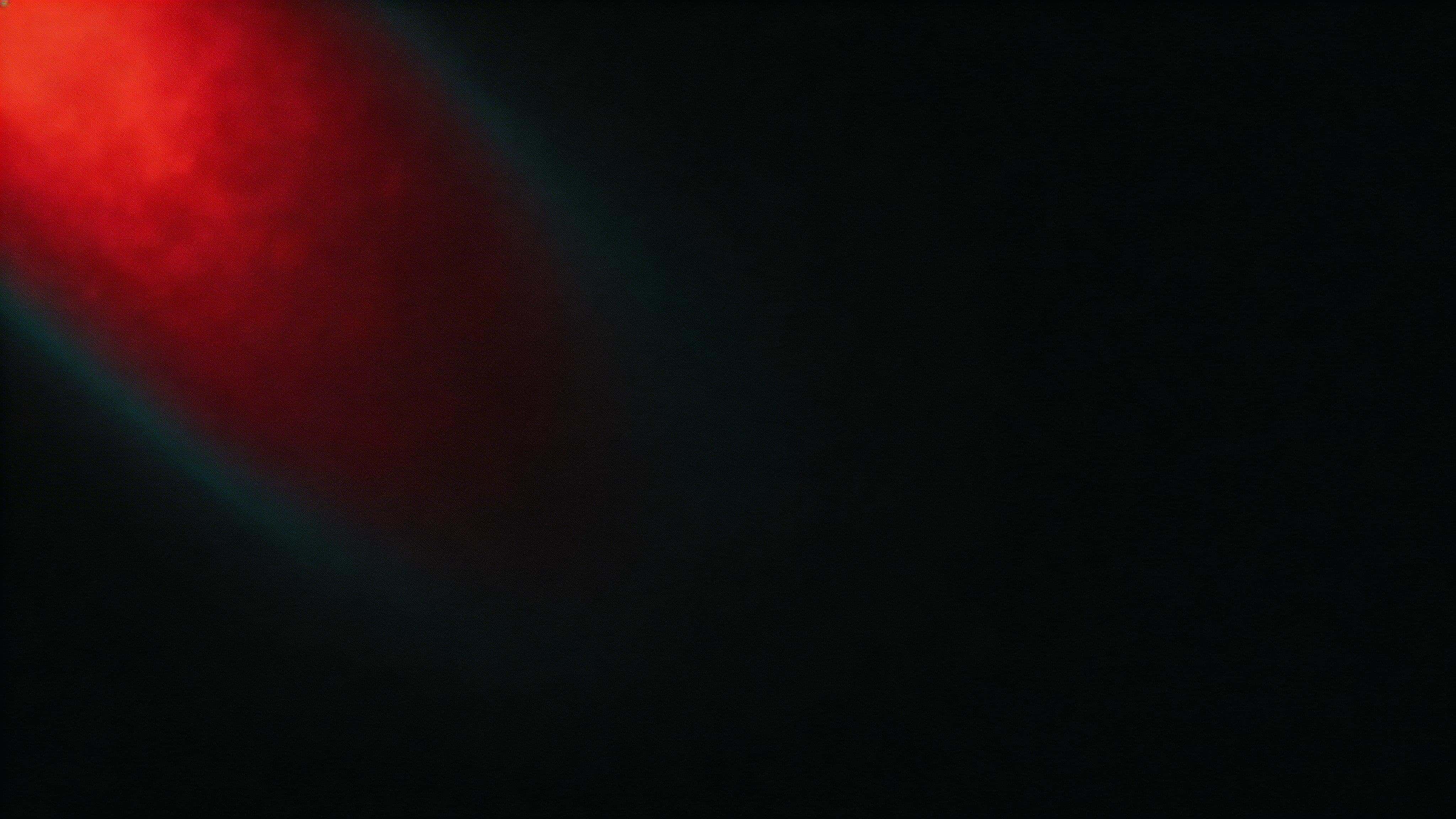 Widescreen 16:9 wallpaper showing an off-center deep crimson glow drifting diagonally into OLED-friendly near-black with ember highlights, a faint cyan-teal fringe, and soft bloom.