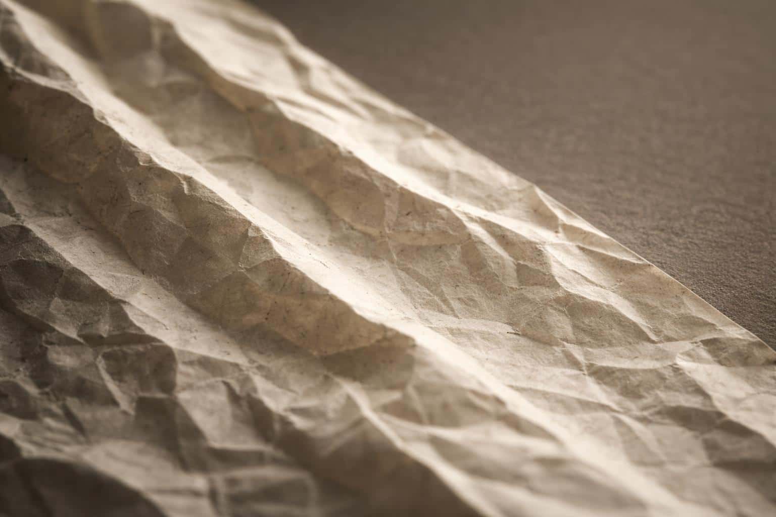 Close-up macro photograph of crumpled paper showing light, shadow and surface grain for use as a textured background or wallpaper in a 3:2 frame.