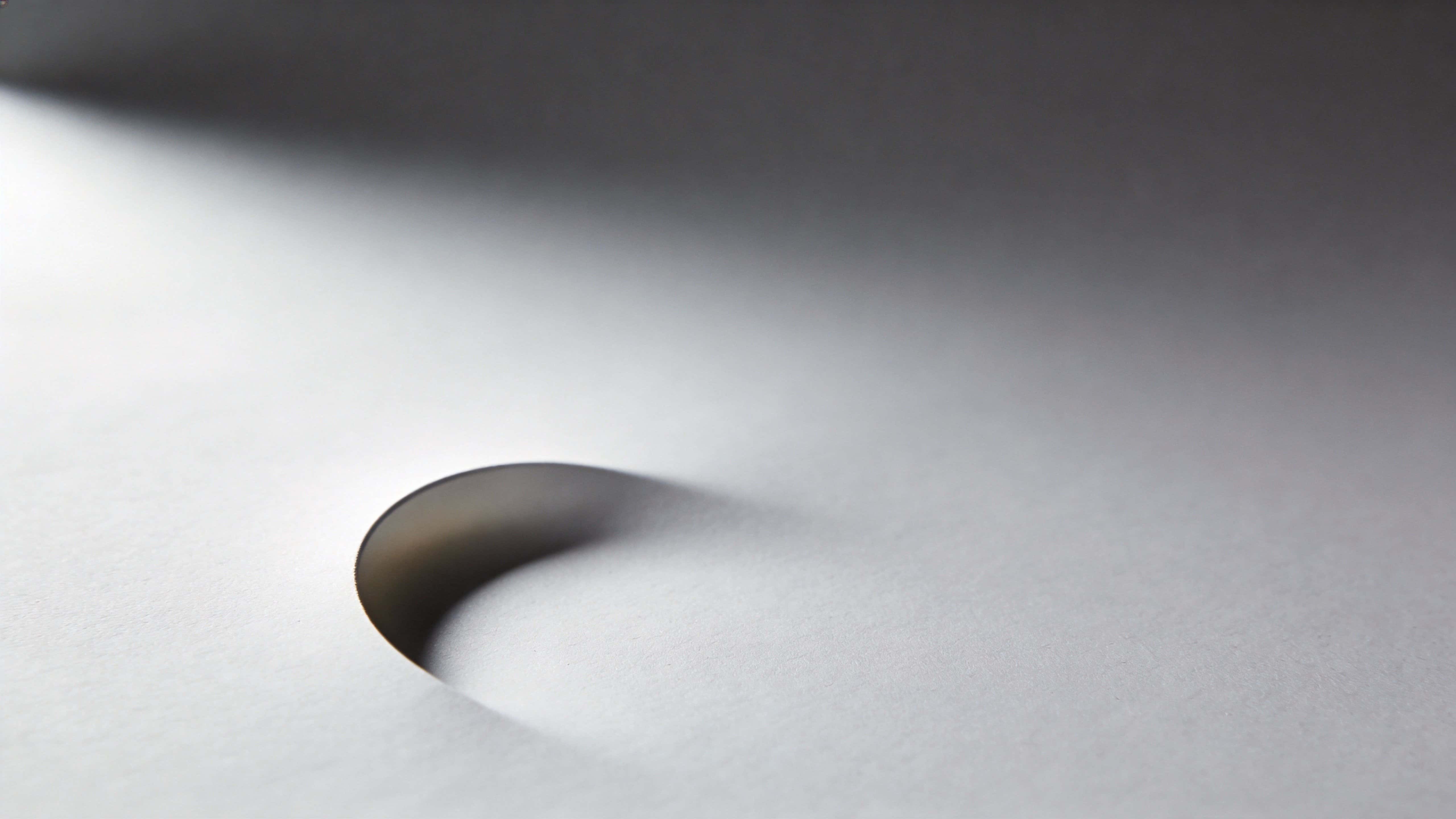 Minimal 16:9 photographic study of a faint curved shadow on a smooth blank background, rendered with soft studio light for editorial or background use.