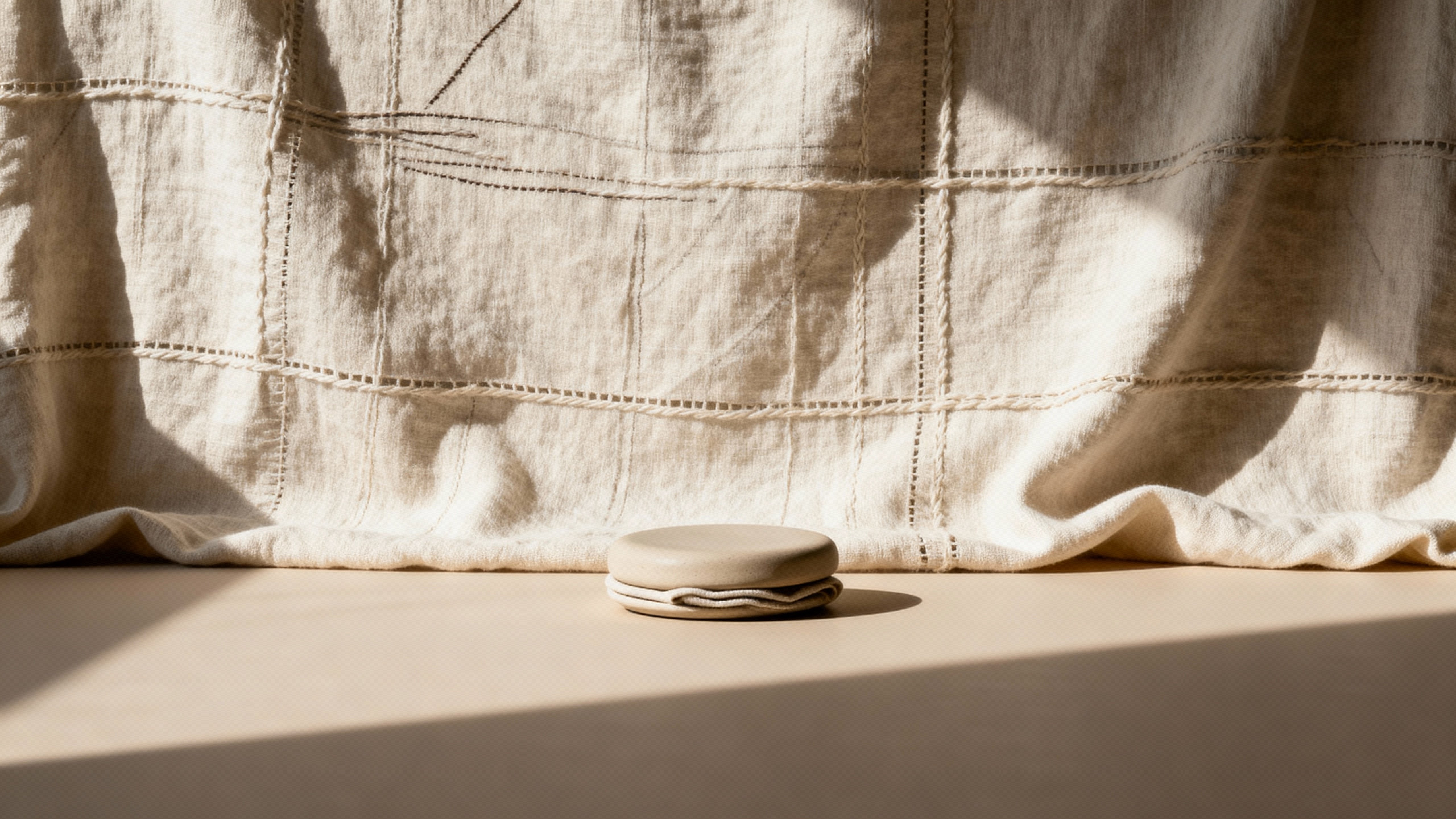 A fabric-like background lit by shallow, directional light that sculpts gentle folds and subtle texture, composed and cropped specifically for a cinematic 16:9 frame.