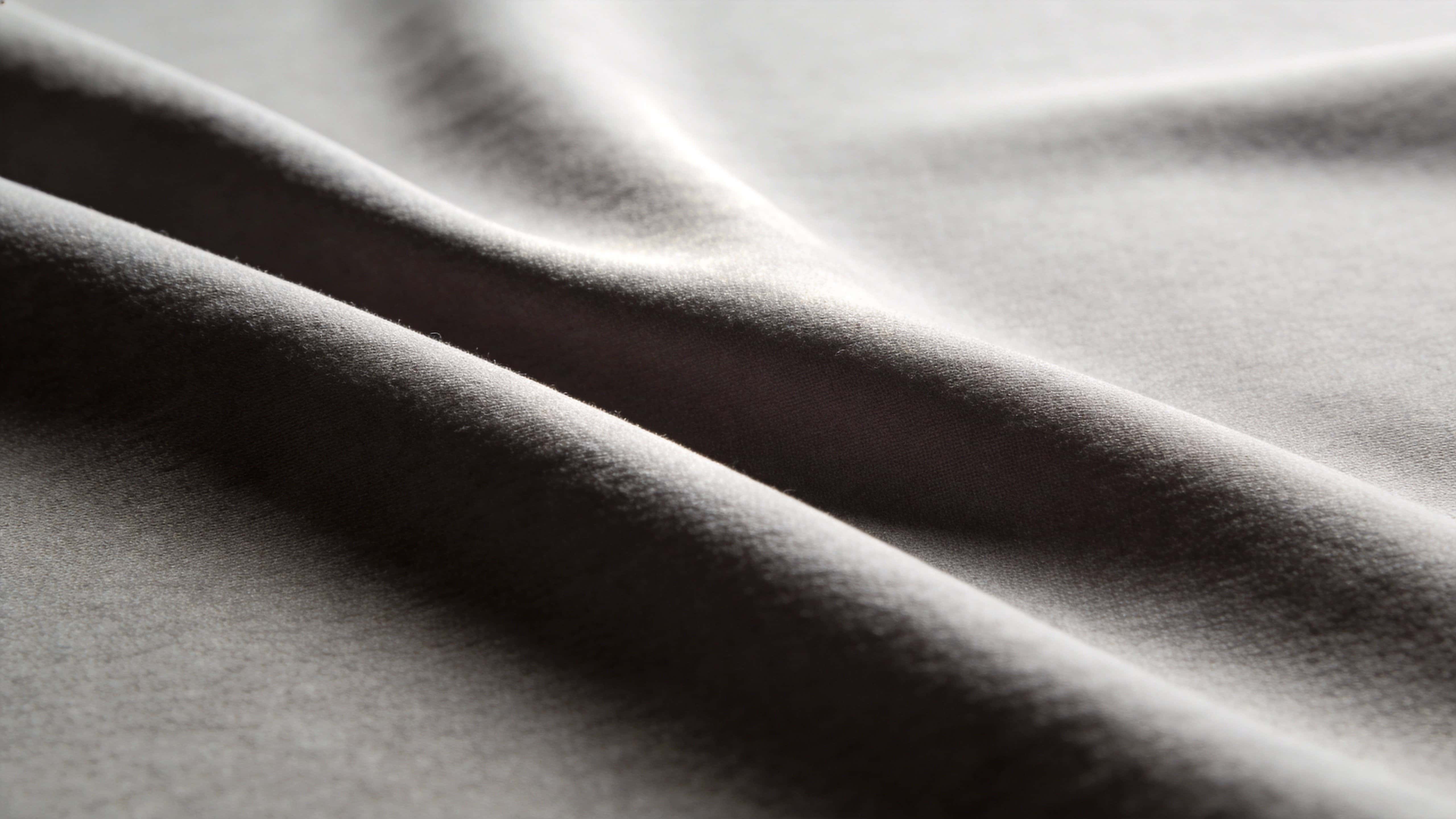 Monochrome study of fabric folds photographed as a widescreen 16:9 composition for wallpaper, emphasizing sculptural texture, soft shadows, and serene minimalism.