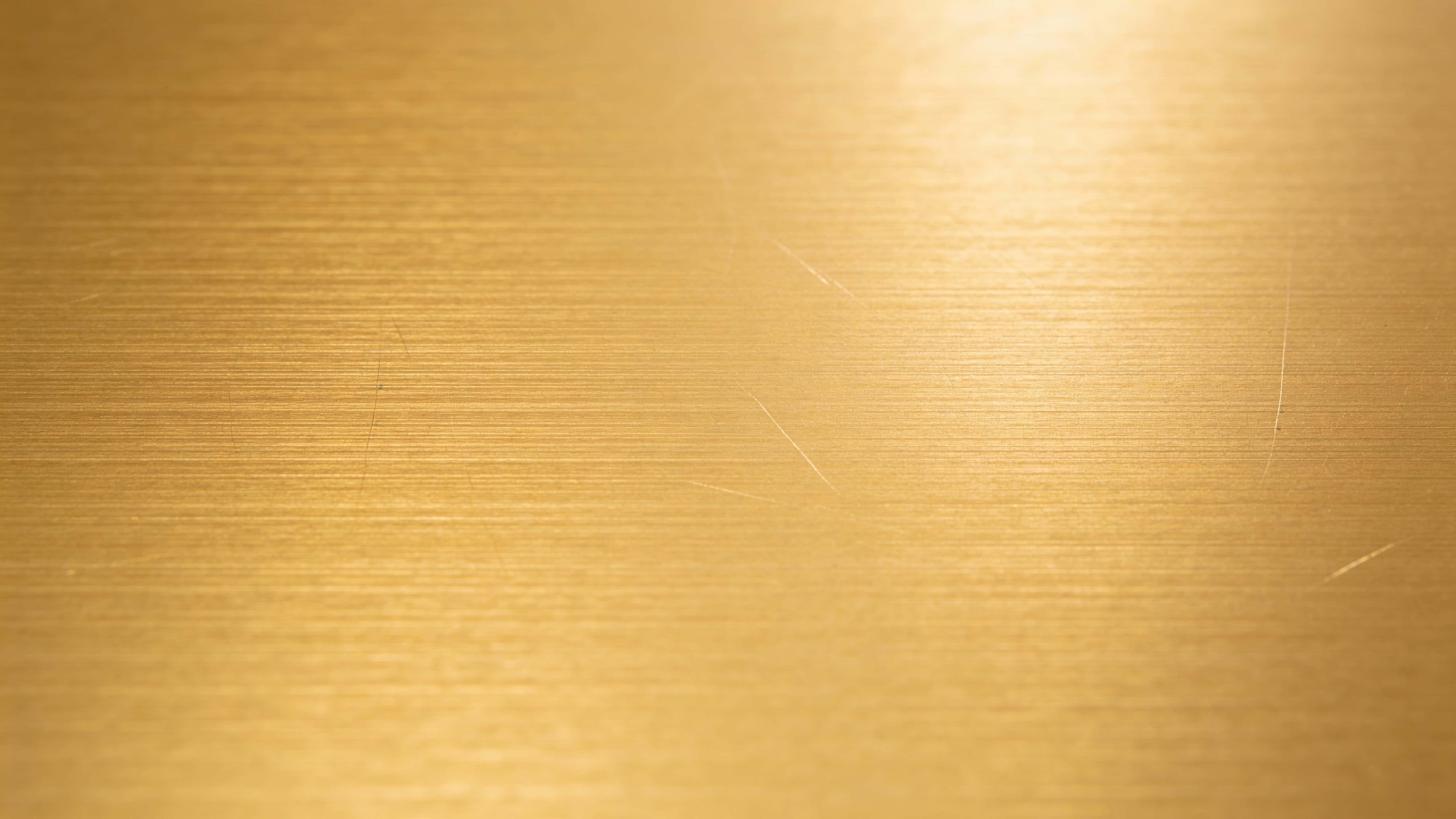 A flat, straight-on champagne gold brushed-metal background with horizontal micro-scratches and soft warm highlights, offering wide clean areas for logos.