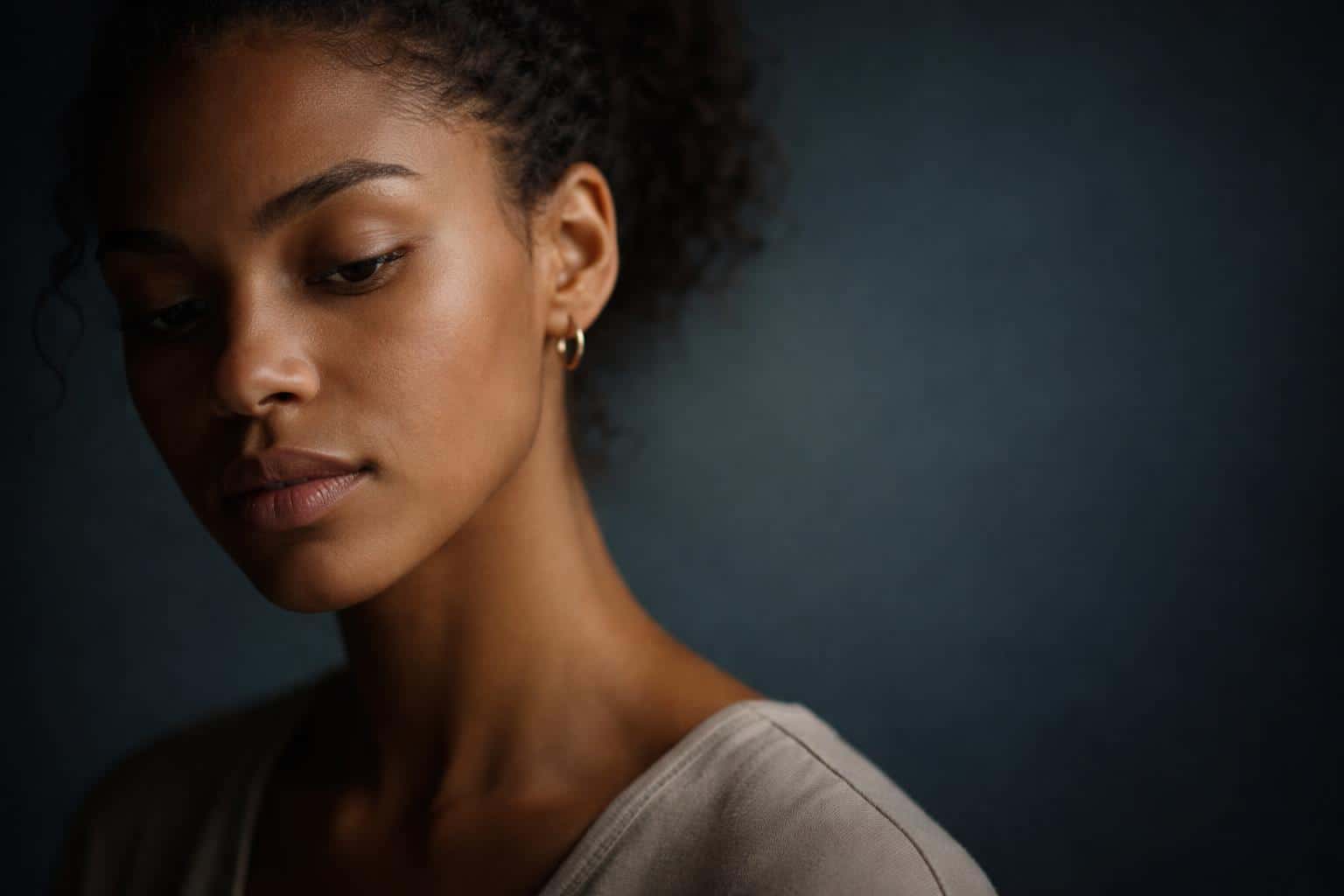 Close 3:2 portrait of a human face turned slightly away, photographed in a low-key, thoughtful mood with soft side light and clean negative space for editorial use.