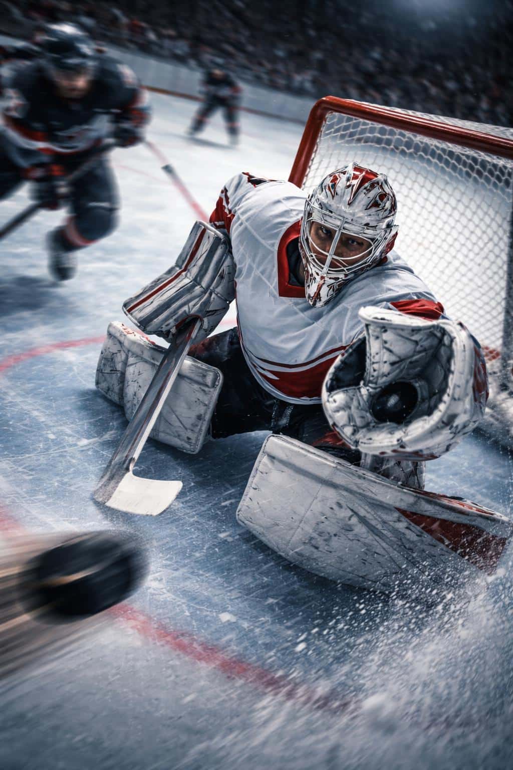 Vertical 2:3 sports photo of an ice-hockey goalie dropping into a sharp save from a high corner angle, frozen crisp against motion-blurred players and puck trail.