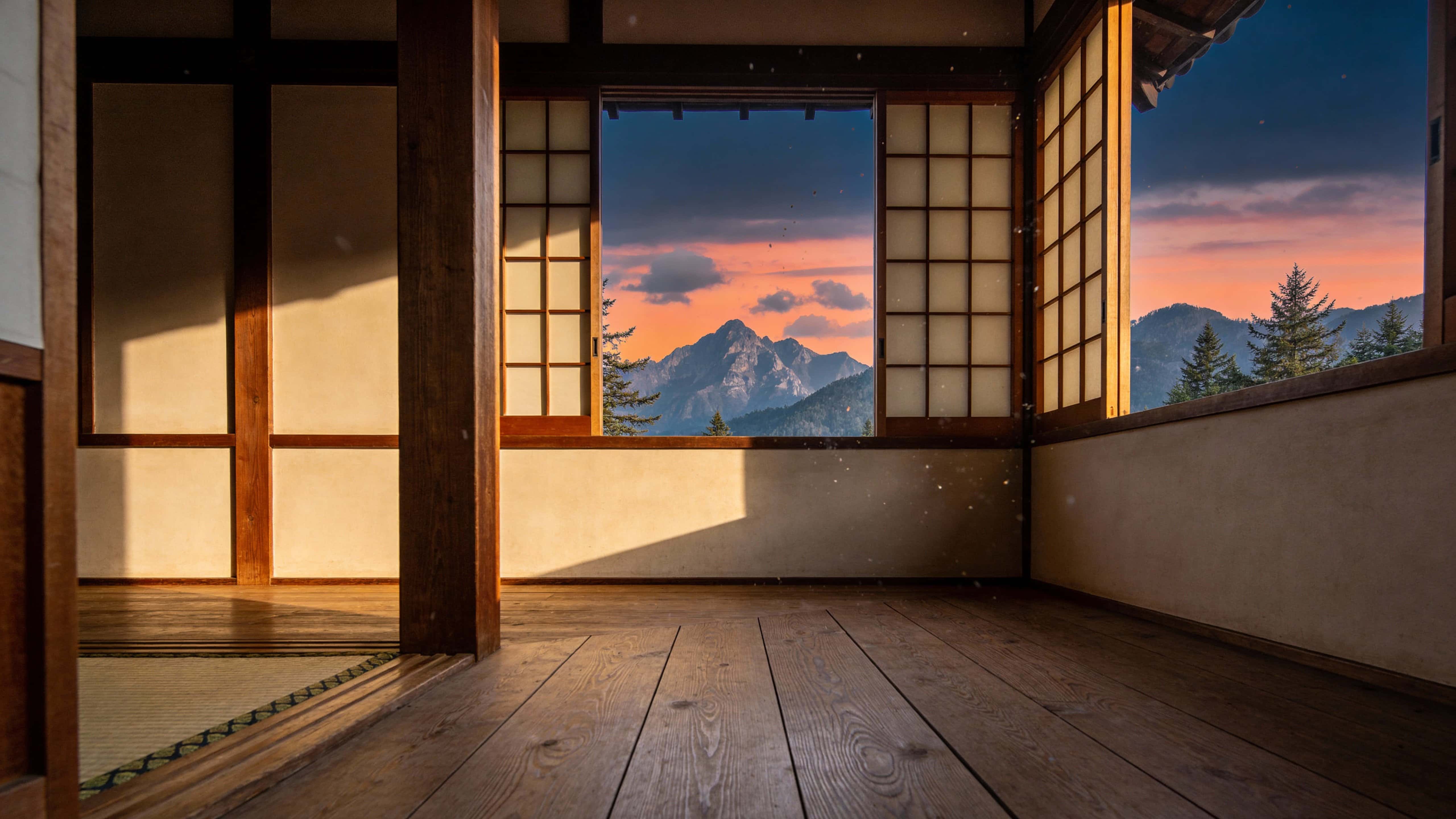 A photorealistic Japanese wooden interior with an open window revealing a sunset-lit mountain landscape, captured in documentary-style realism with soft ambient light and neutral color grading, framed in a wide 16:9 aspect ratio.