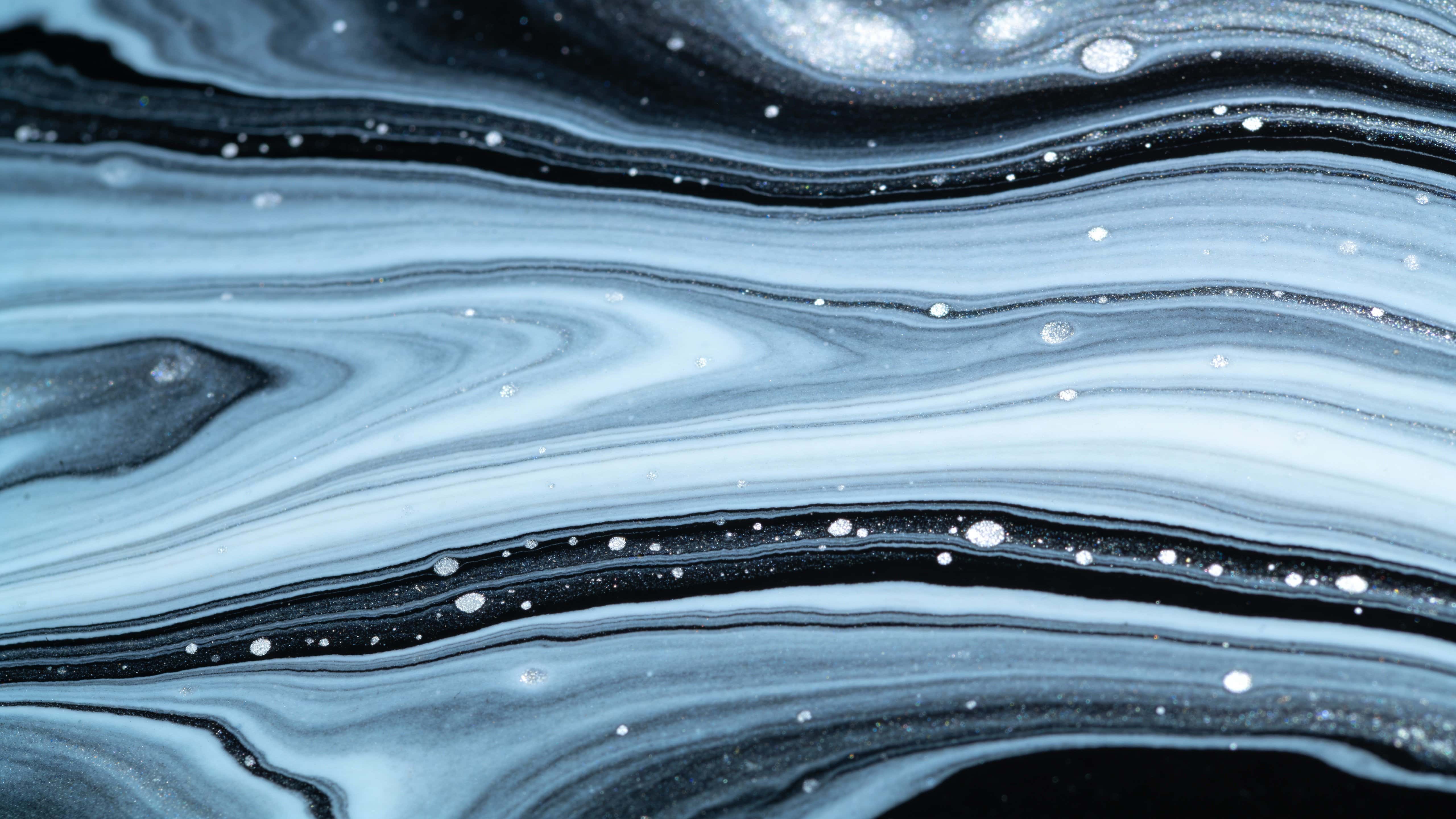 A full-frame close-up of a marbled fluid surface with layered swirls, veined bands, thin channels and fine white speckles across cool slate tones, rendered as a tactile photographic texture.
