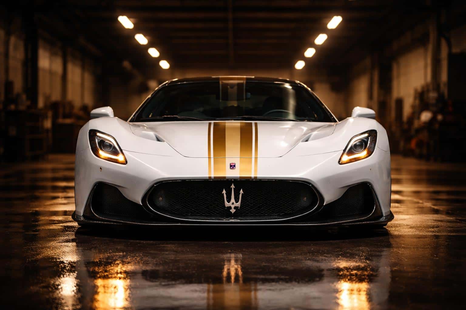 Front-facing Maserati supercar photographed in an industrial garage, glossy white with gold accents and warm reflections, framed for a 3:2 poster-cover composition.