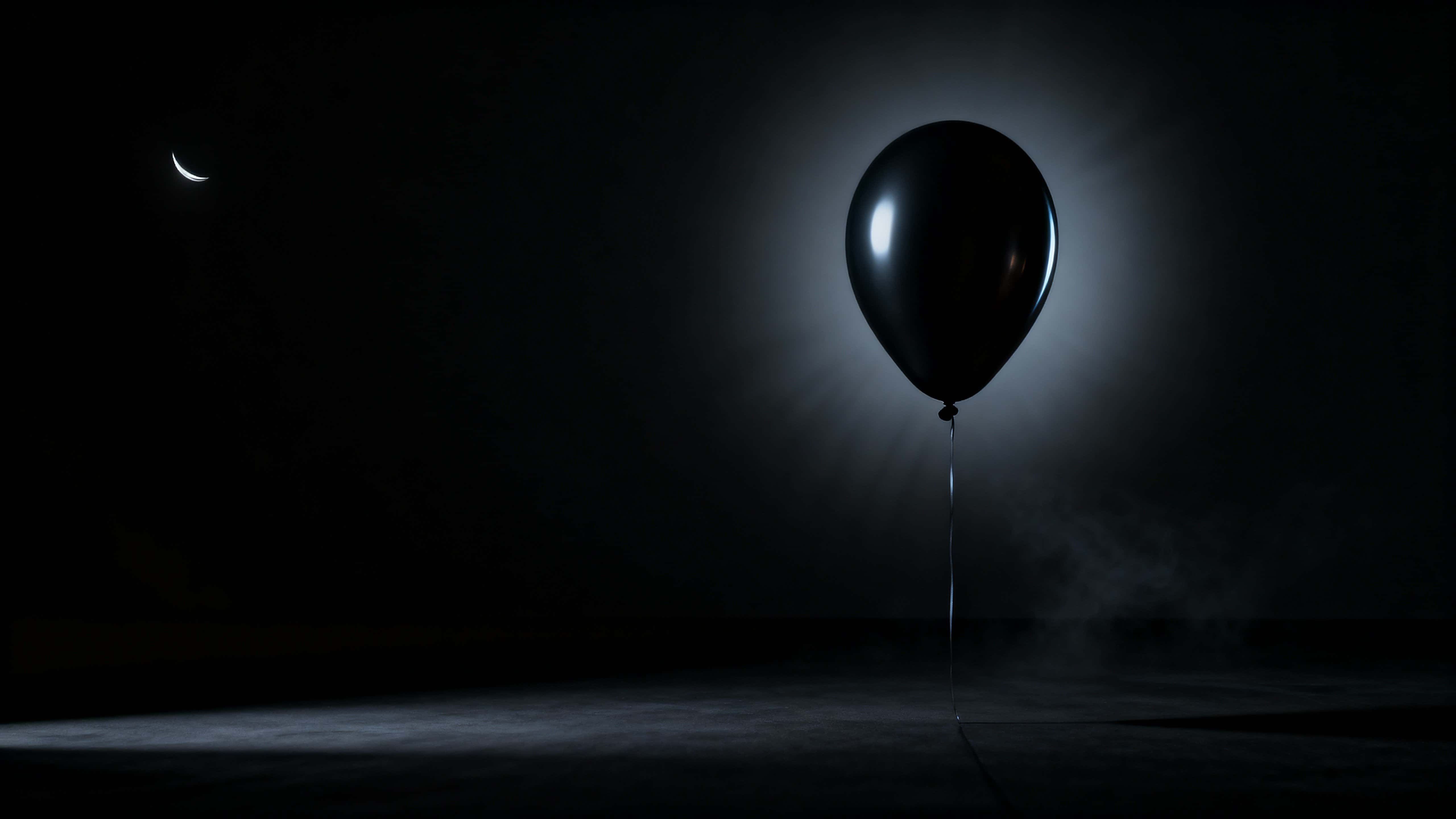 A matte-black teardrop balloon drifts from the lower-right toward center in 16:9, rim-lit by a cool crescent revealing soft rubber texture that fades into velvety shadow with subtle haze.