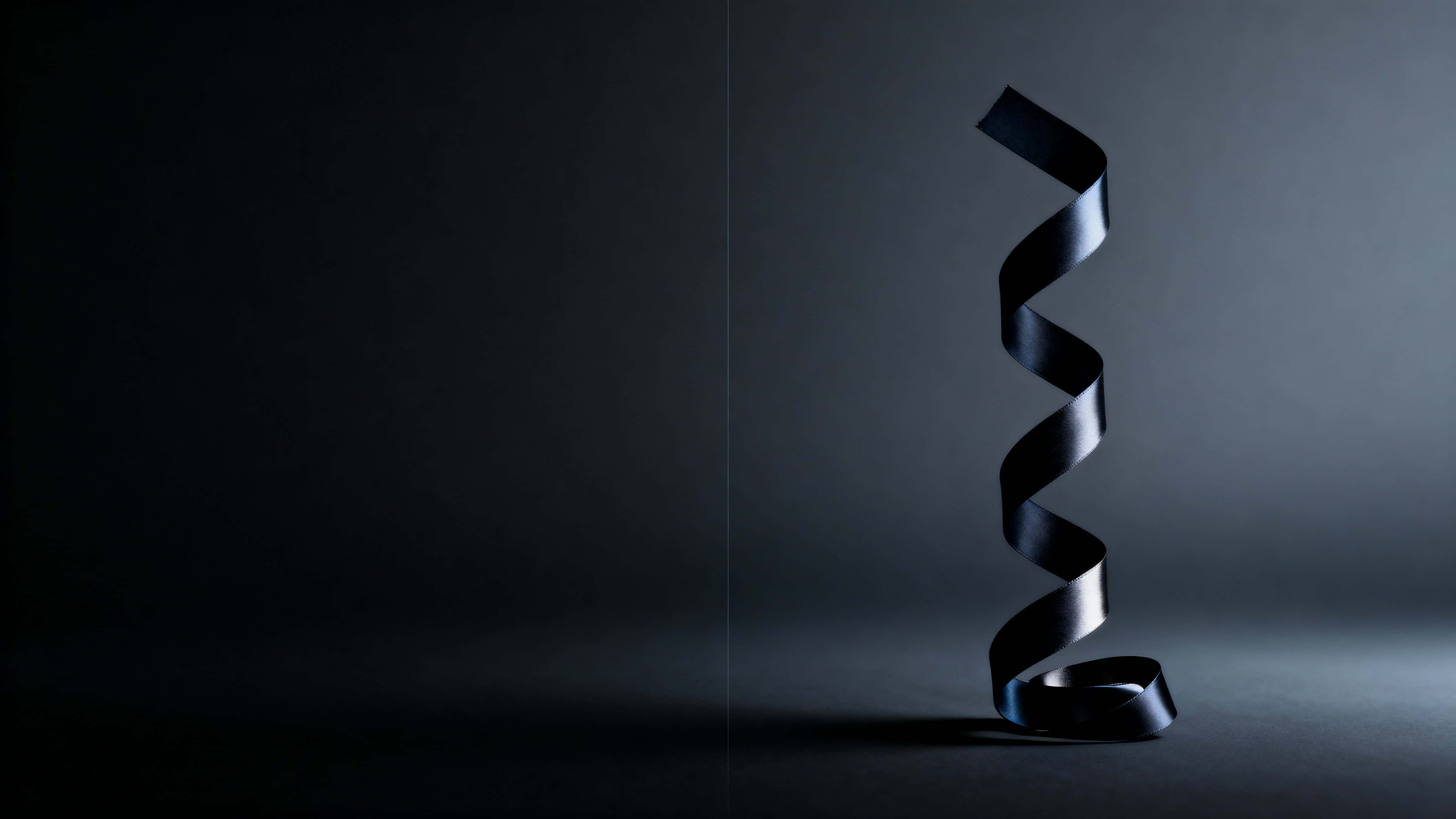A matte-black ribbon twists upward on the center-right of a 16:9 frame, defined by soft upper-left rim light against expansive near-black negative space and subtle haze.