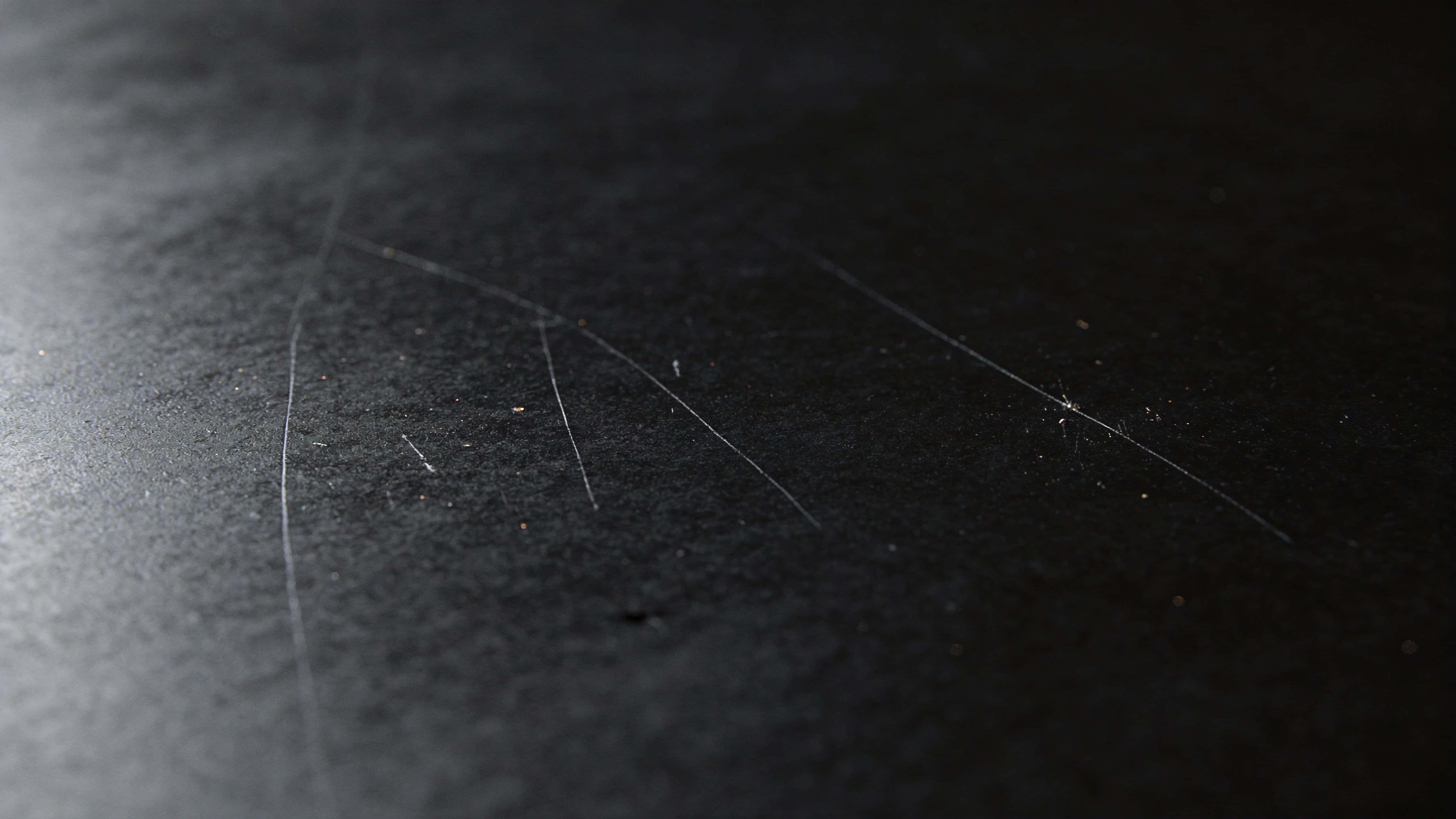 Close-up product-style study of a matte black surface with fine scratches, photographed for background or wallpaper use with moody minimalist lighting and texture focus.
