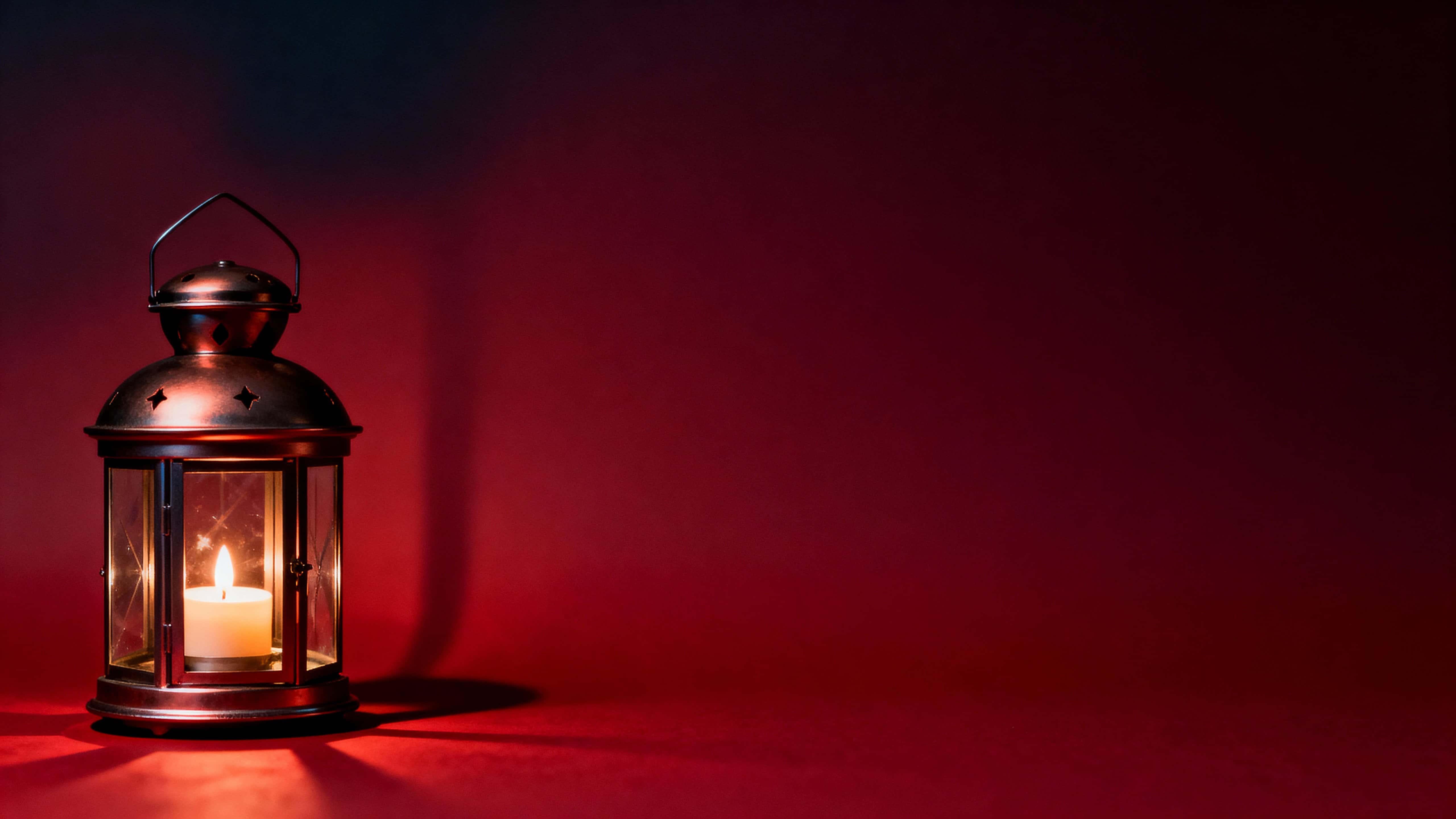 A 16:9 Christmas-card scene shows a single deep-red metal lantern with glass panels at the left third, emitting a warm candlelike glow against a smooth dark crimson gradient background.