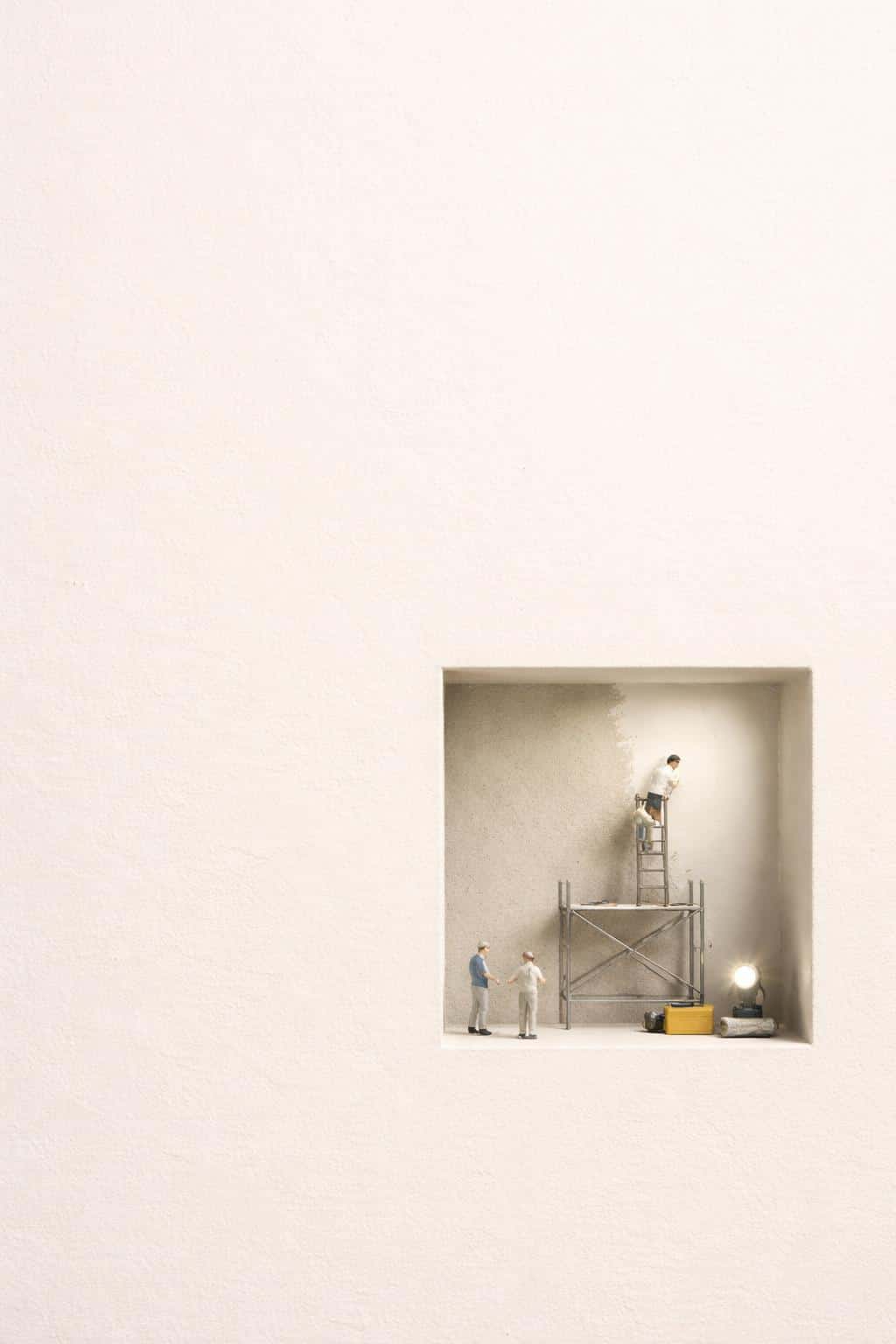 Portrait 2:3 scene of a minimal warm off-white paper surface with a small recessed cutout in the lower third revealing a miniature worksite with tiny workers, scaffold, and neat tools.