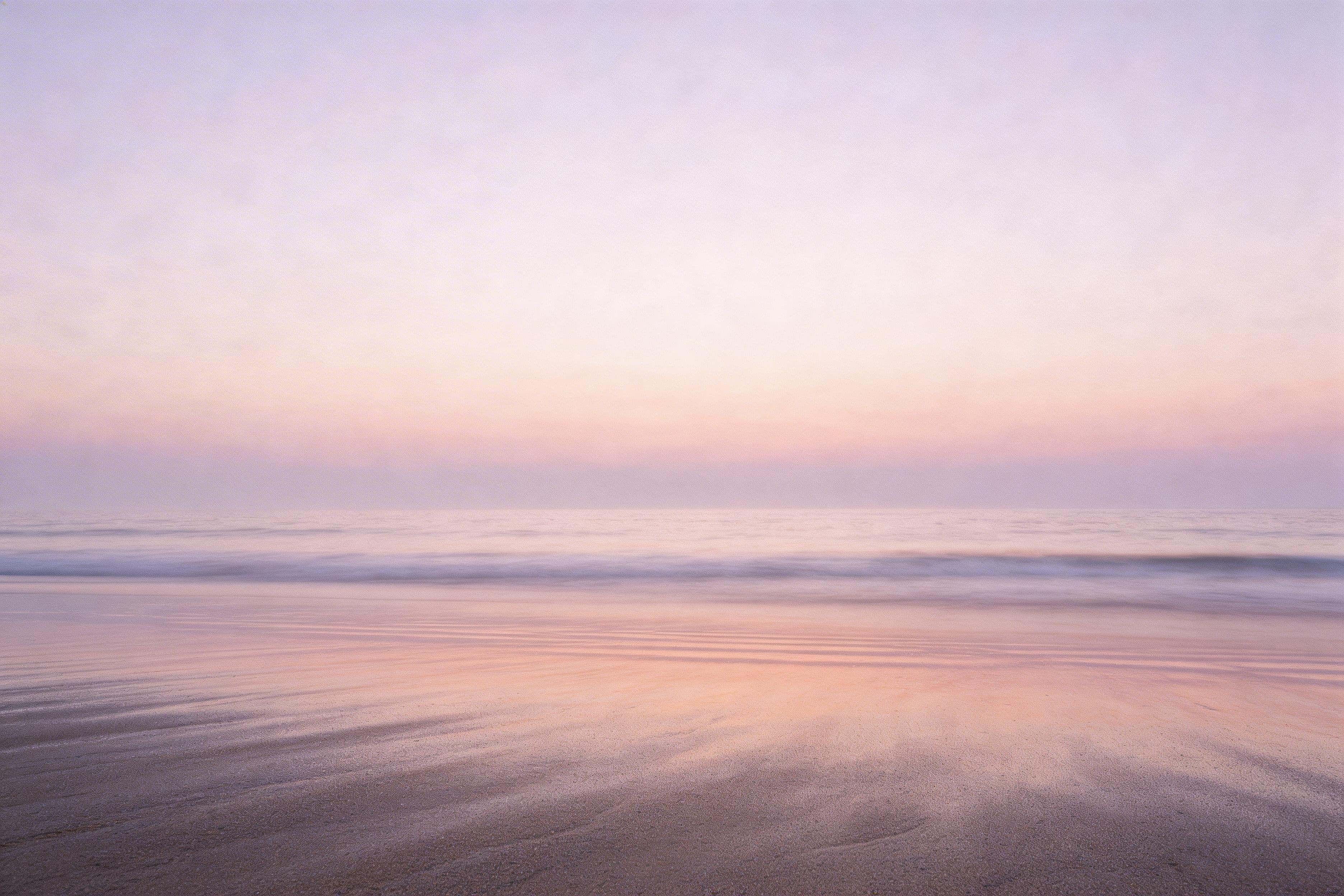 Cinematic editorial 3:2 photograph of a minimal sunrise beach with a low stable horizon, soft sea mist, broad negative sky, and smooth wet sand reflecting a pastel dawn gradient with subtle film grain and realistic texture.