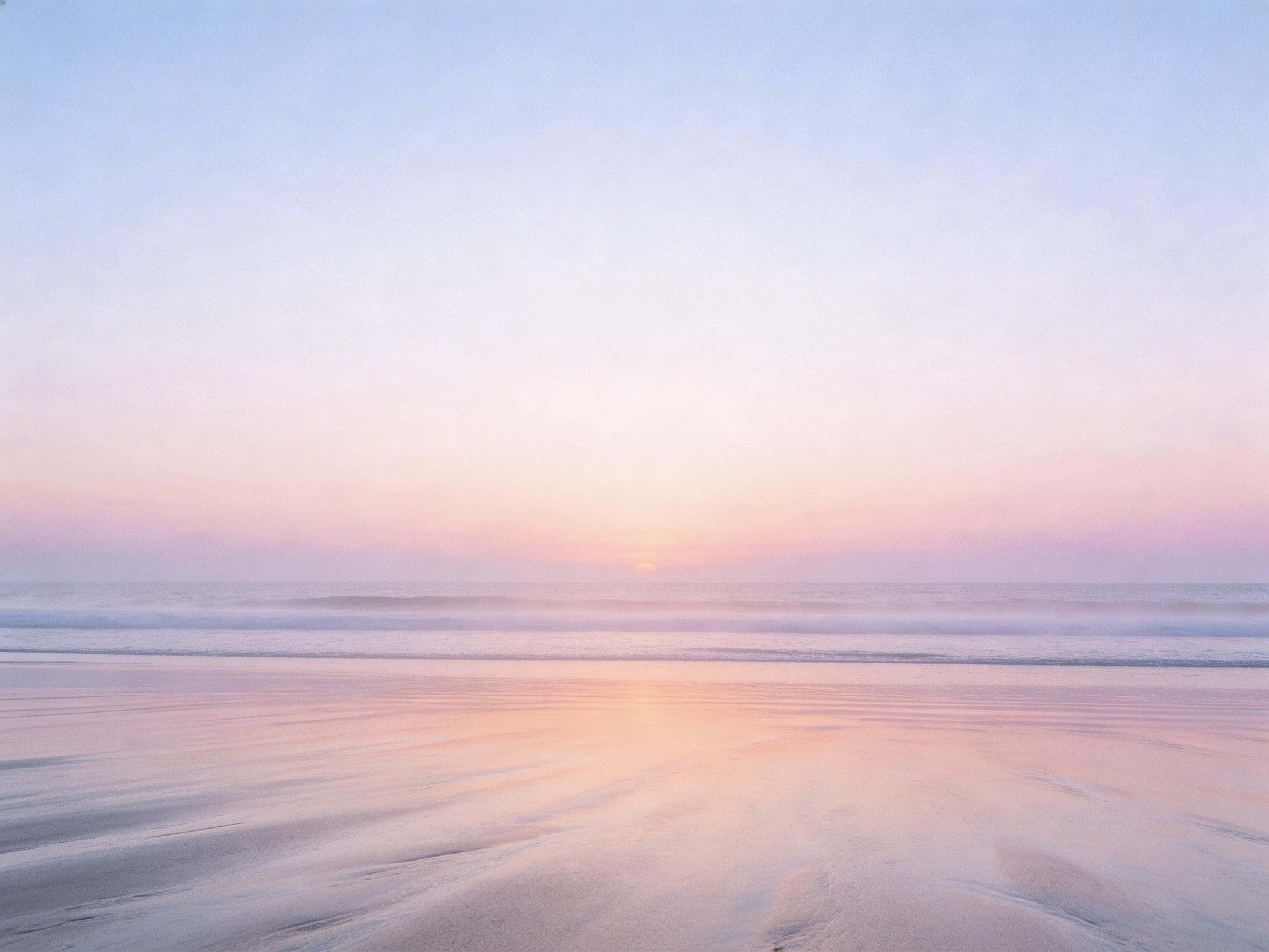 Cinematic 4:3 editorial photograph of a minimal sunrise beach with a low stable horizon, soft sea mist, smooth wet sand reflecting a pastel dawn gradient and subtle film grain.