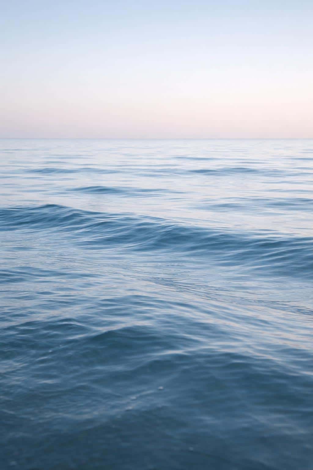 Vertical 2:3 minimalist ocean horizon scene in soft cool light for a serene wallpaper or poster, featuring calm waves, restrained palette, and generous negative space.