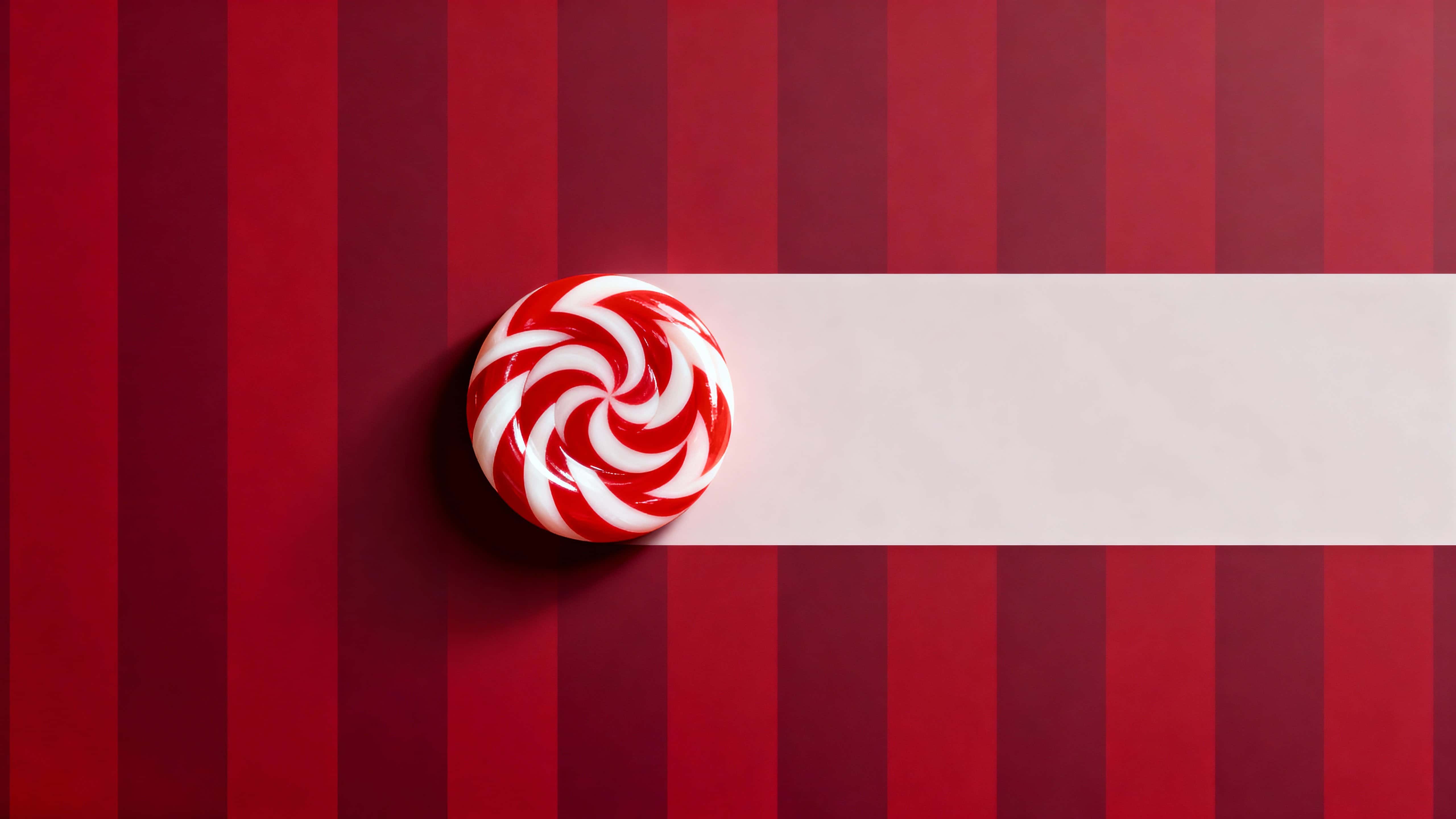 A minimalist 16:9 Christmas scene featuring a glossy red-and-white peppermint candy positioned near the left third against a deep burgundy gradient background with calm right-side copy space.