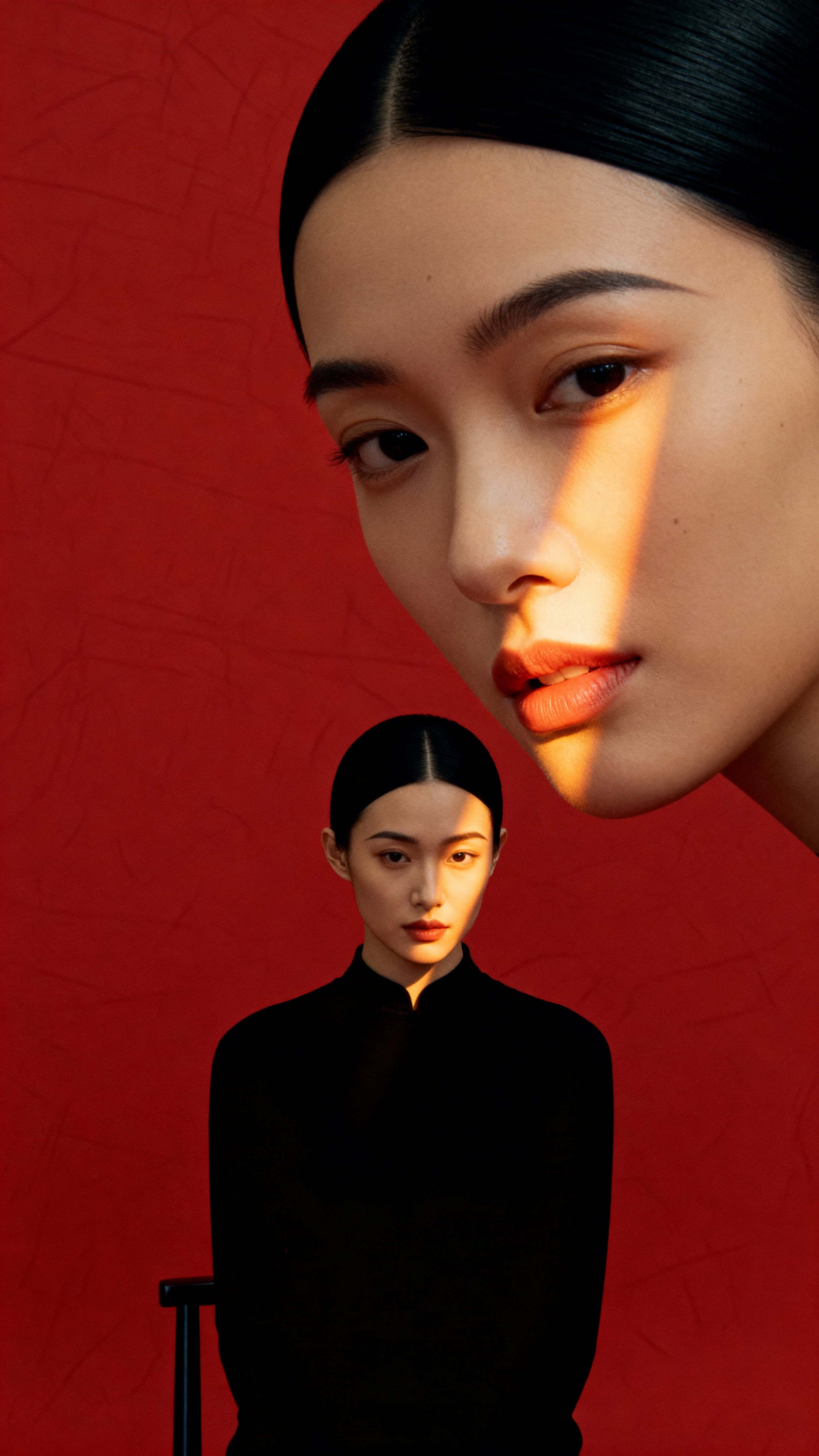 A standing person framed within a 9:16 red field creates a bold vertical silhouette with black clothing and hair, while a warm diagonal light sculpts the face and emphasizes lips and the nose bridge.