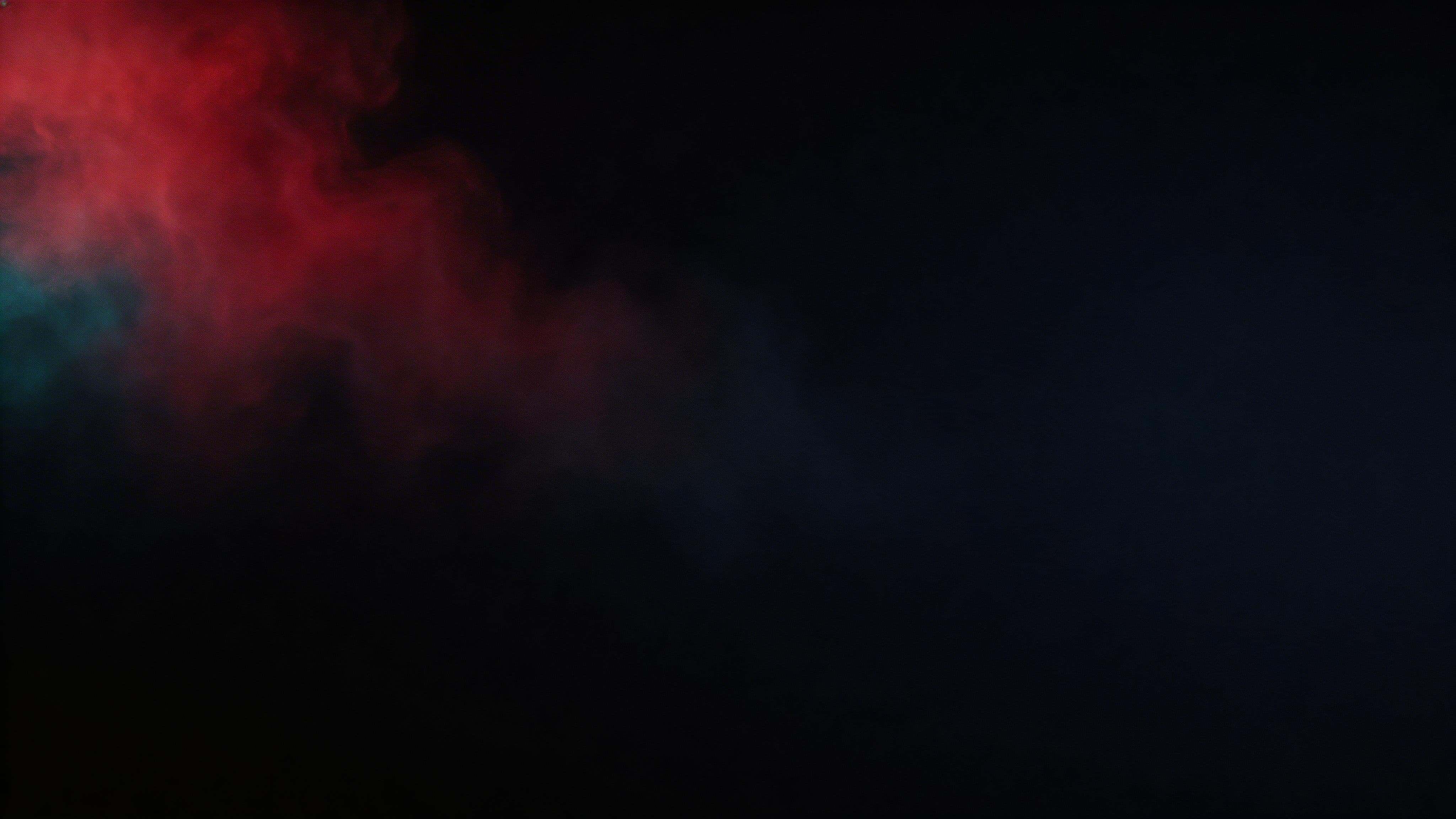 A 16:9 widescreen wallpaper showing a left-third pocket of red gel-lit fog drifting diagonally across deep navy-black negative space with cyan-teal edge shimmer and subtle film grain.