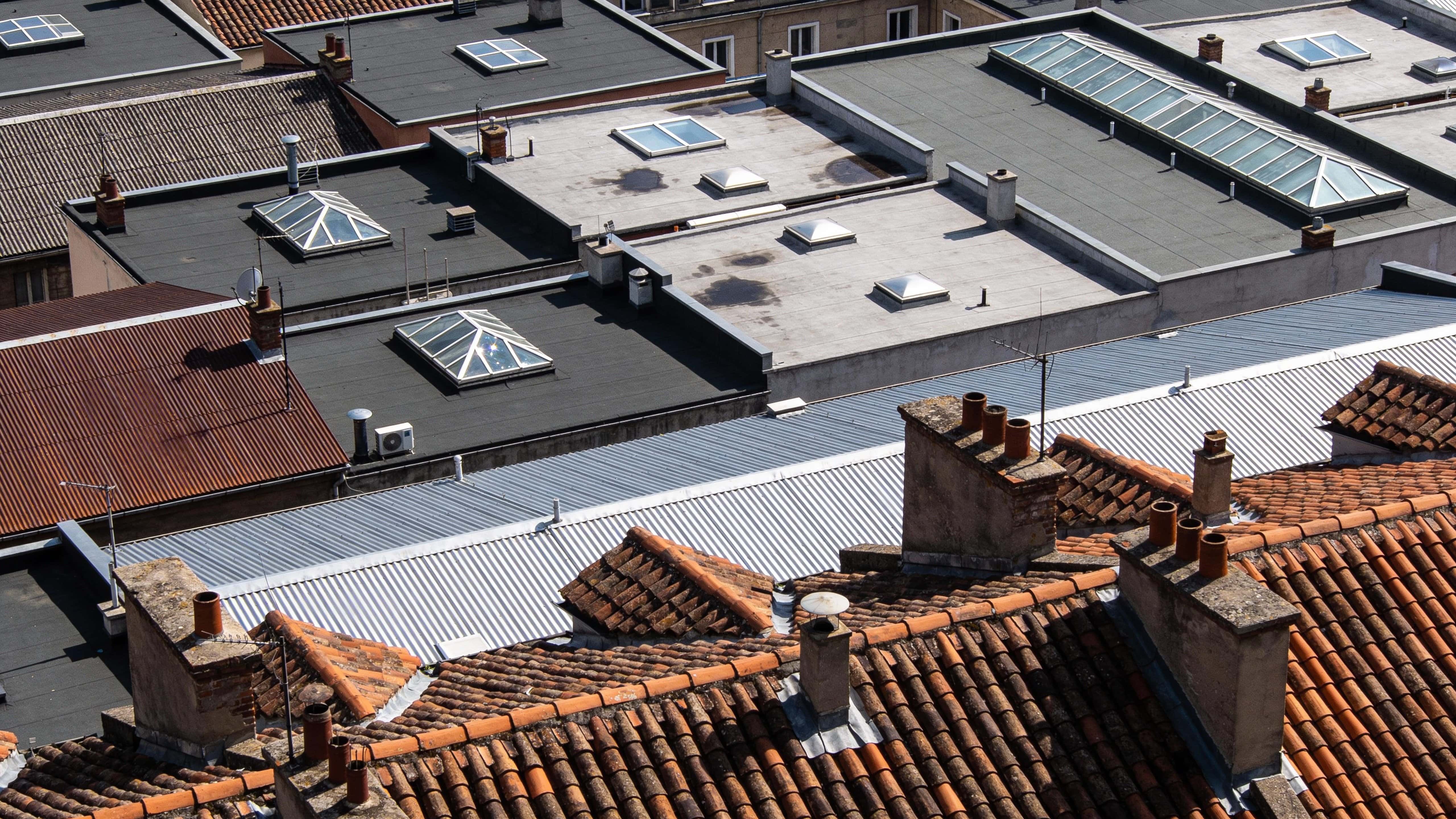 Aerial architectural photograph of urban rooftops framed in a 16:9 ratio, emphasizing geometric roofs, vents, skylights and textures with a clean overhead composition for wallpaper.