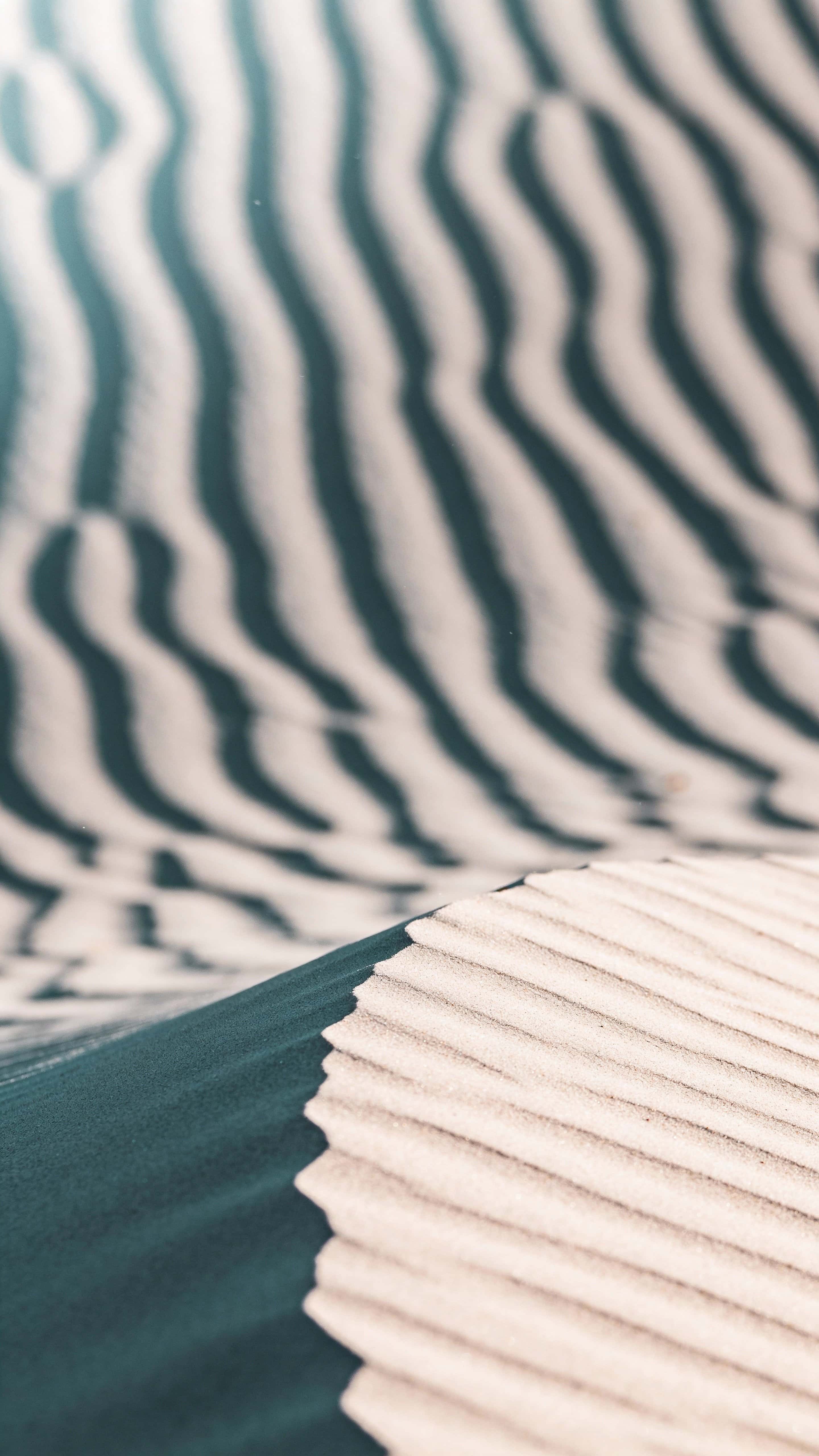 Close-up vertical 9:16 study of sand ripples filling the frame with diagonal curving bands of muted teal and soft off-white, shallow depth of field, matte granular texture.