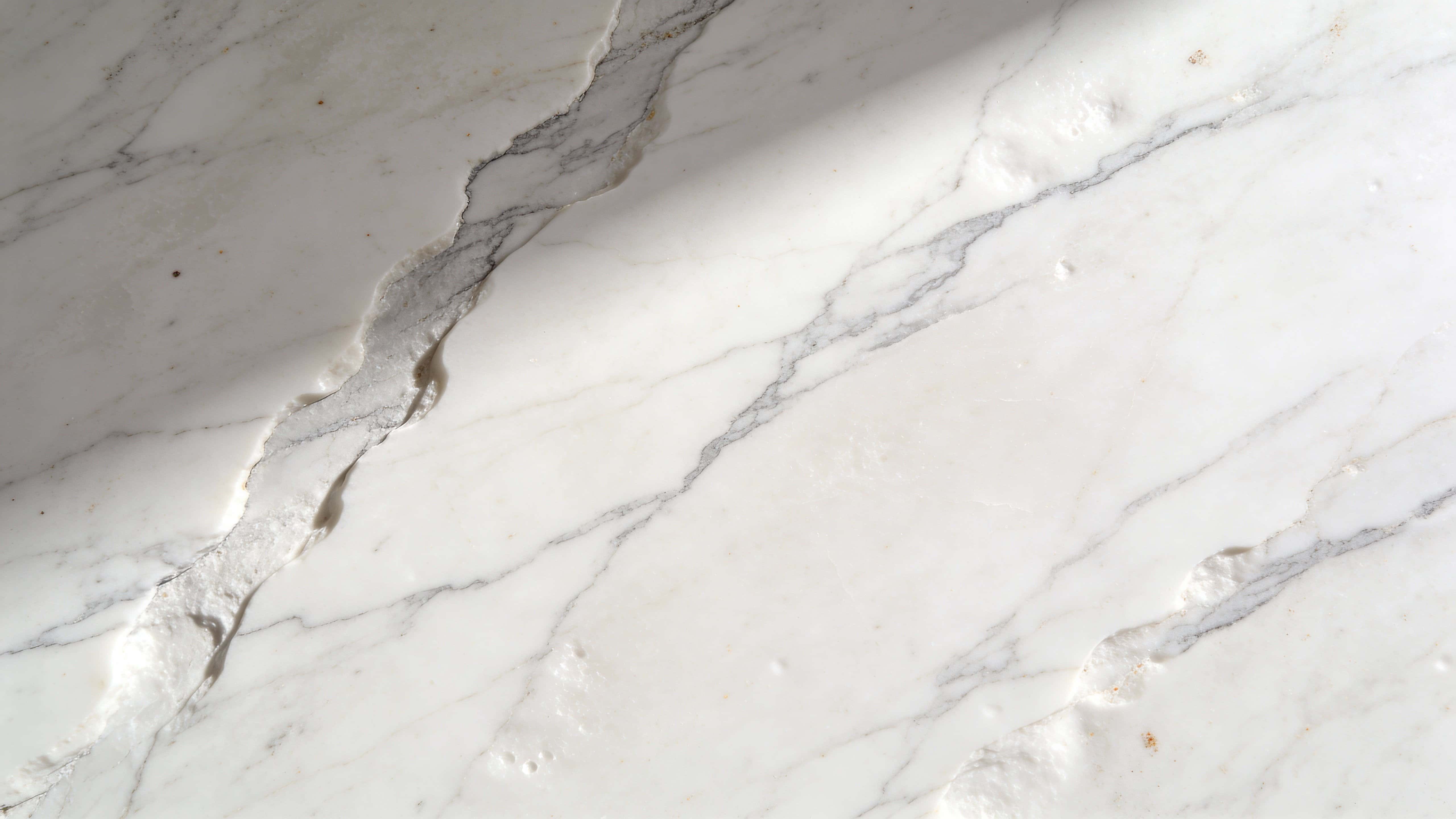 Top-down 16:9 photograph of a white marble surface with subtle gray veins, soft directional light, and minimal composition designed for clean wallpaper backgrounds.