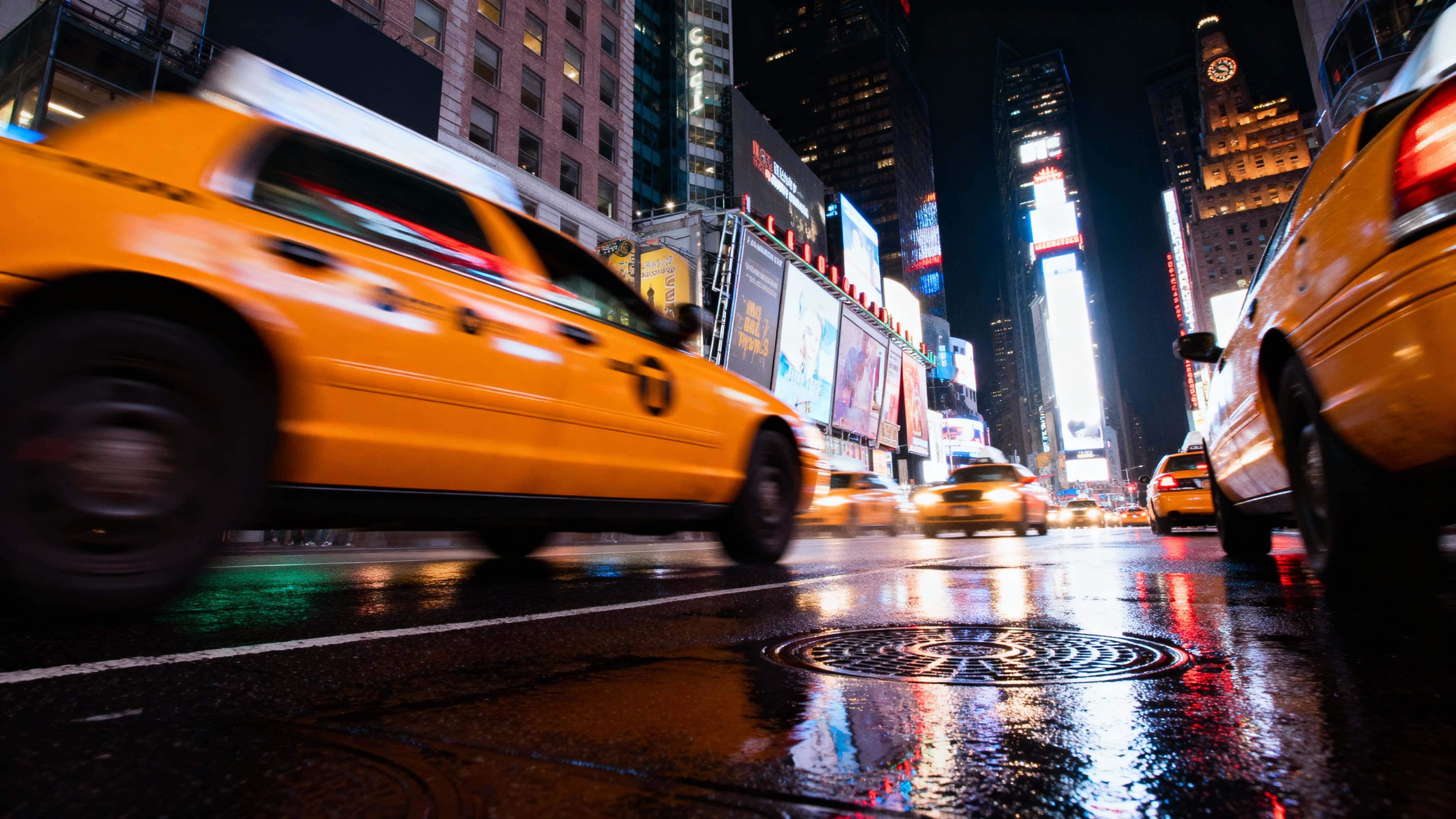Long-exposure night view of yellow taxis streaking through Times Square with vivid neon reflections on realistic wet pavement and cinematic motion blur in 16:9.